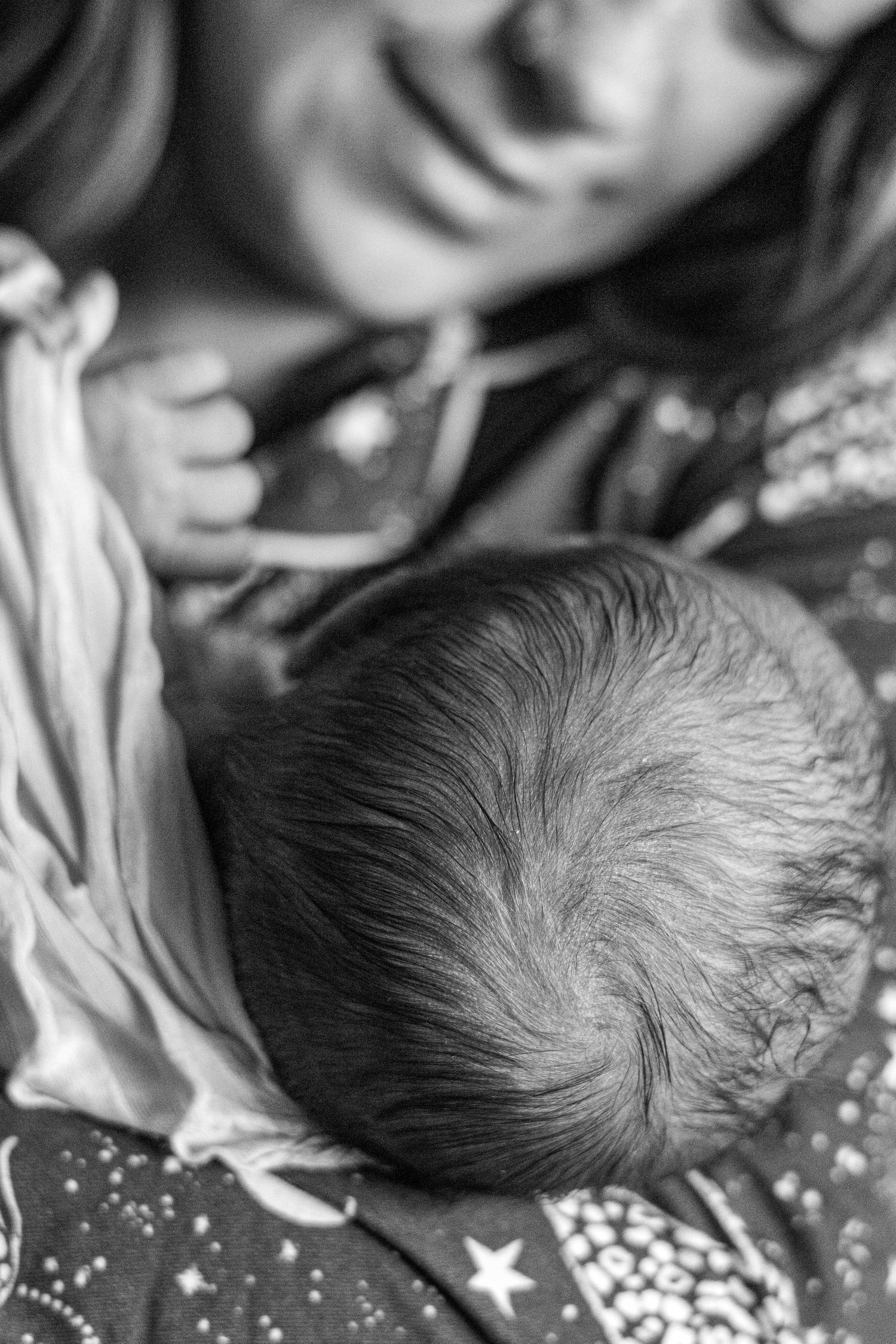 Smiling mother gazing lovingly at newborn baby\u2019s head, black and white birth photo.
