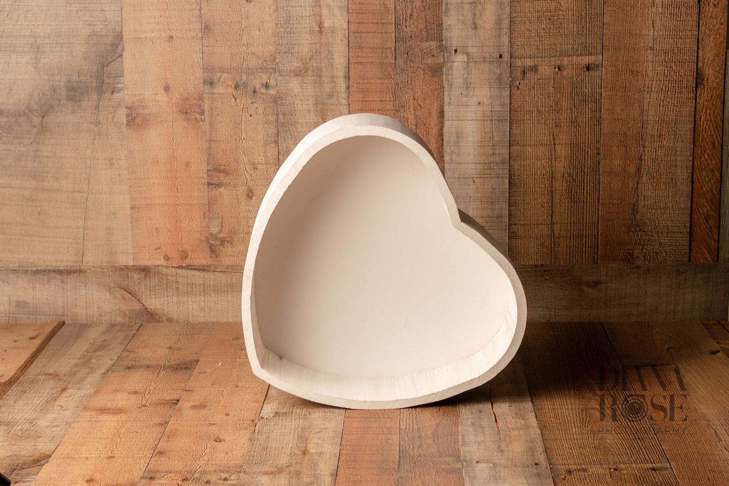 White heart-shaped wooden bowl displayed against a rustic wood plank background on a natural wood floor.