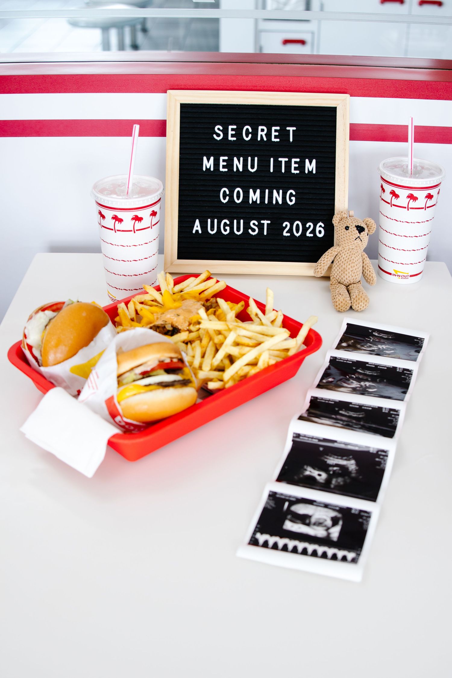 In-N-Out Burger tray with burgers and fries beside ultrasound photos and a sign reading Secret Menu Item Coming August 2026.