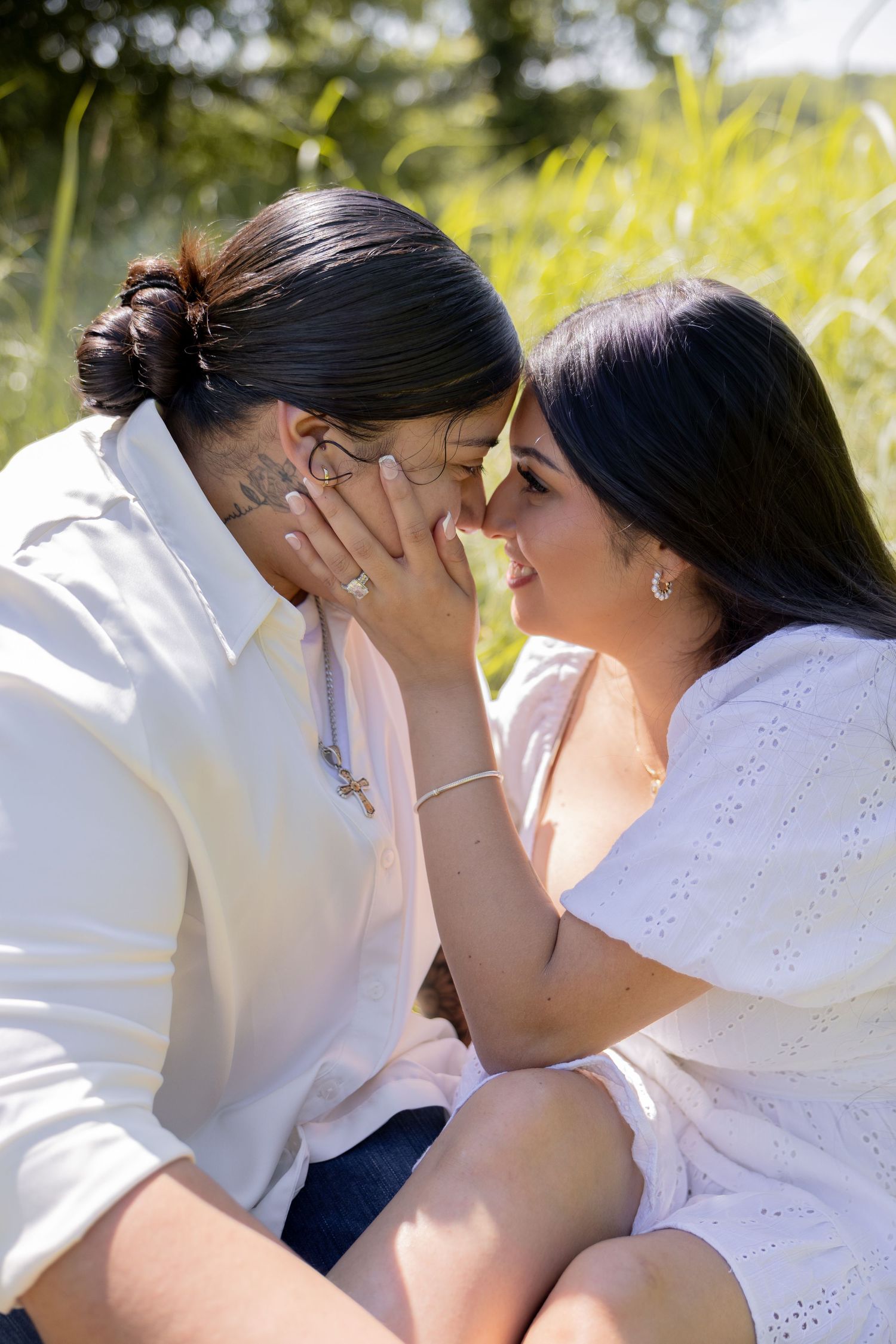 Couple sharing an intimate forehead-to-forehead moment while sitting in a sunny outdoor grassy setting.