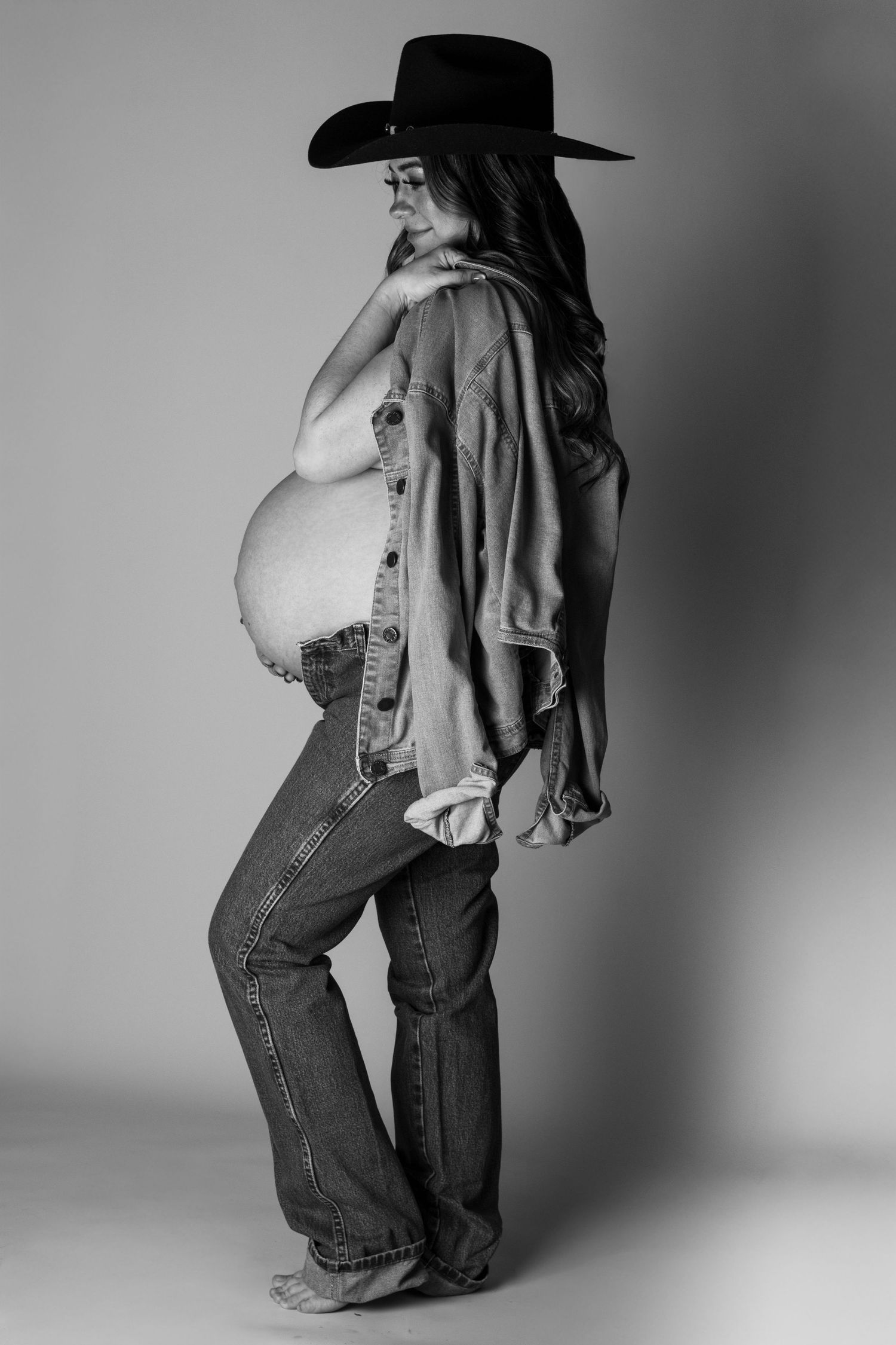 Black and white maternity photo of a pregnant woman in jeans and cowboy hat showing baby bump.