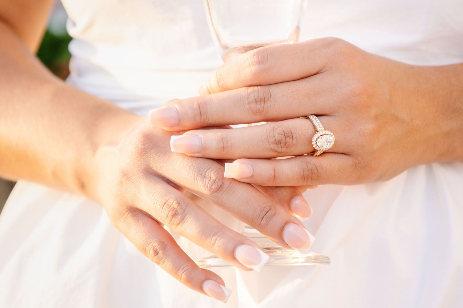Close-up of bride's hands showing a elegant bezel-set engagement ring on her finger.