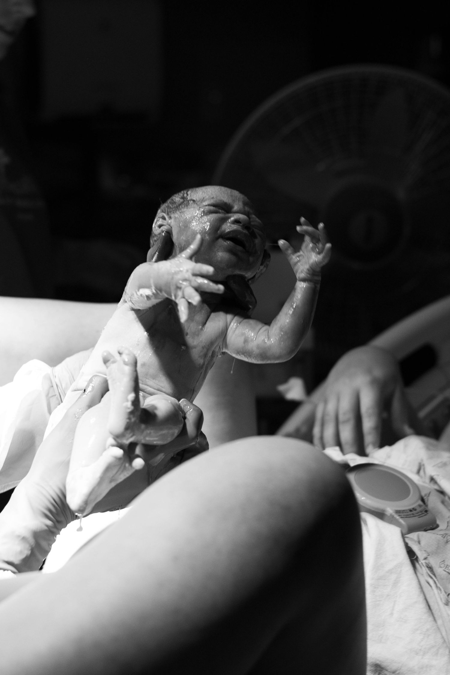 Black and white photo of a newborn baby crying moments after birth being held by medical staff.