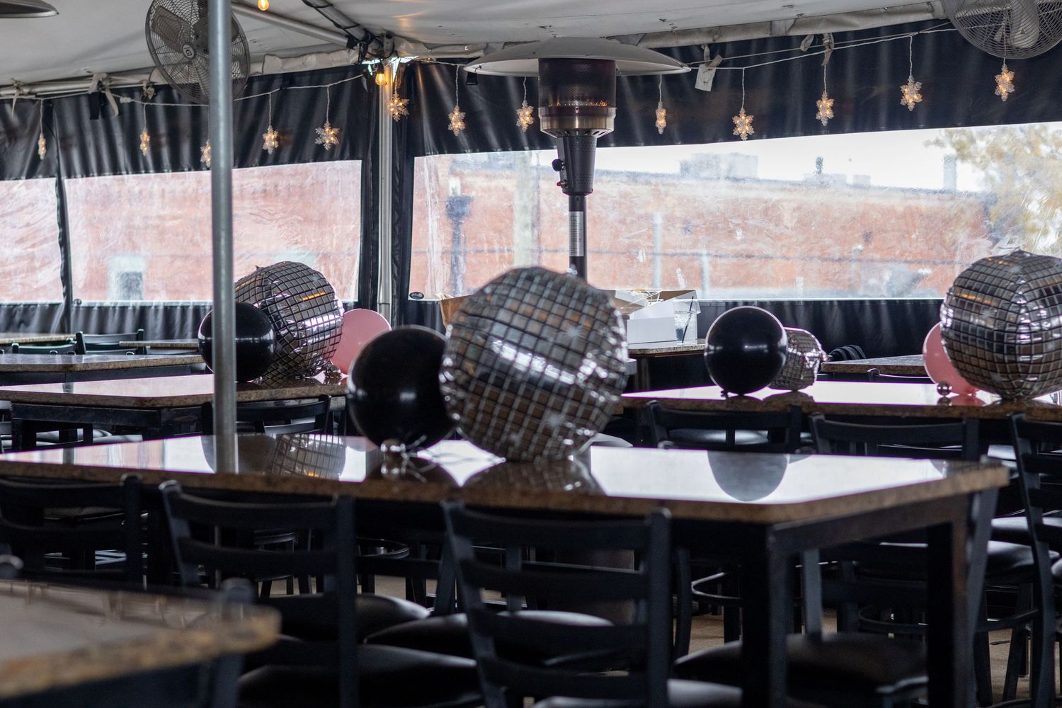 Empty covered patio restaurant with disco ball centerpieces on dark wood tables and chairs.
