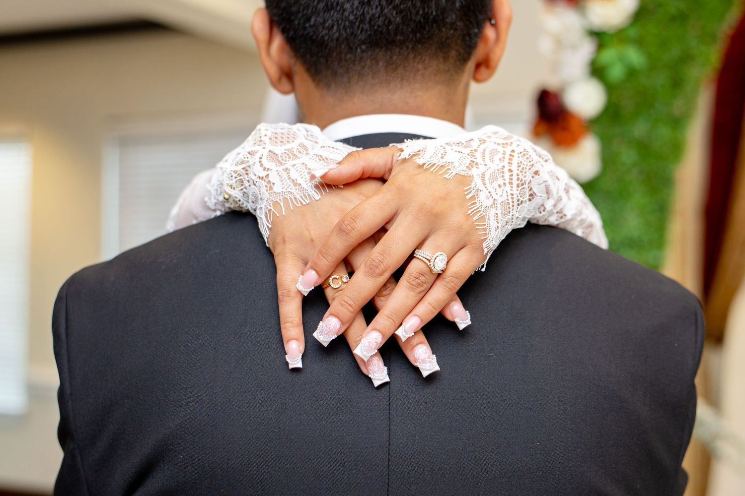 Close-up of bride's hands with engagement ring resting on groom's shoulders during wedding embrace.