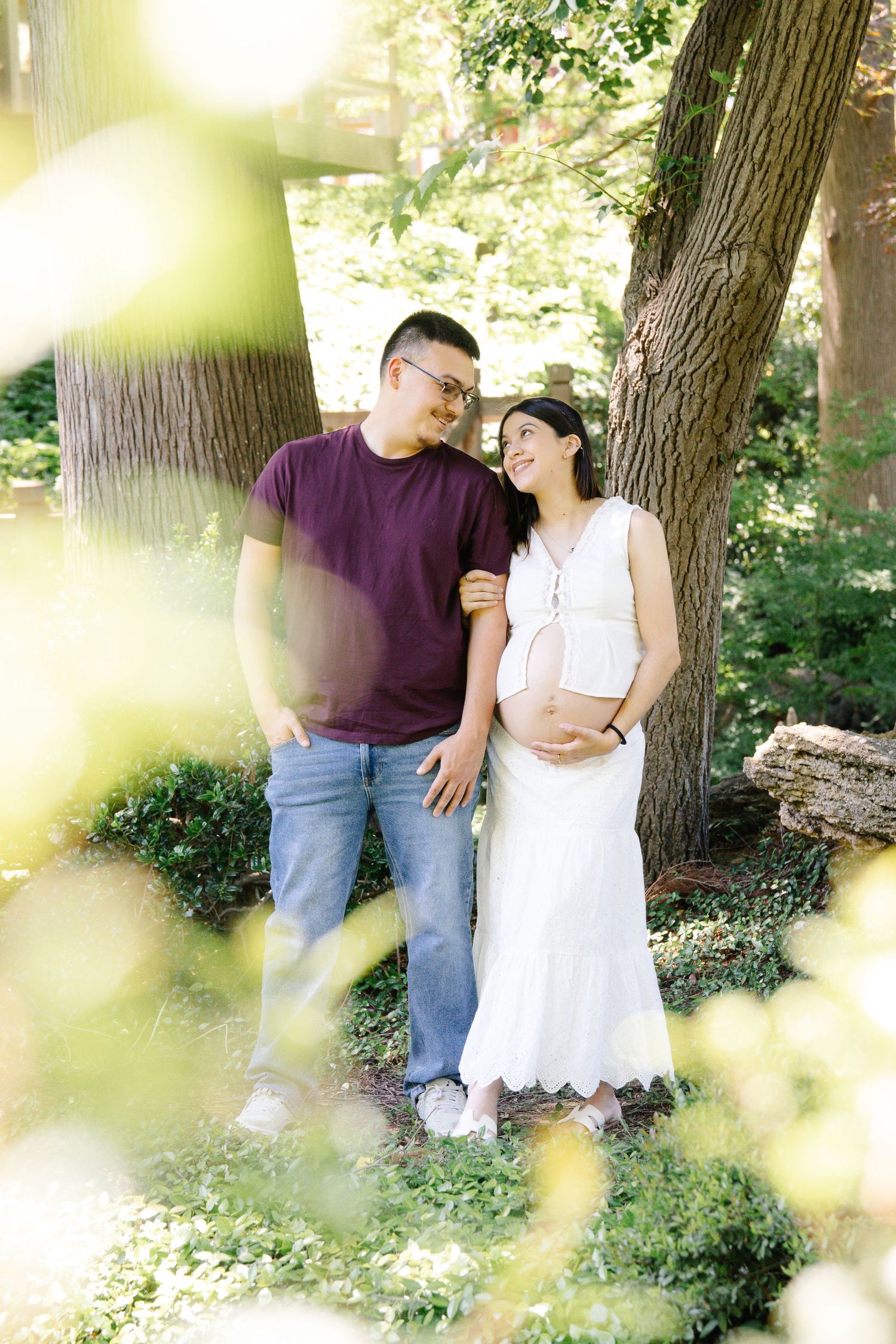 Happy expecting couple sharing a joyful smile together in a lush green outdoor garden setting.