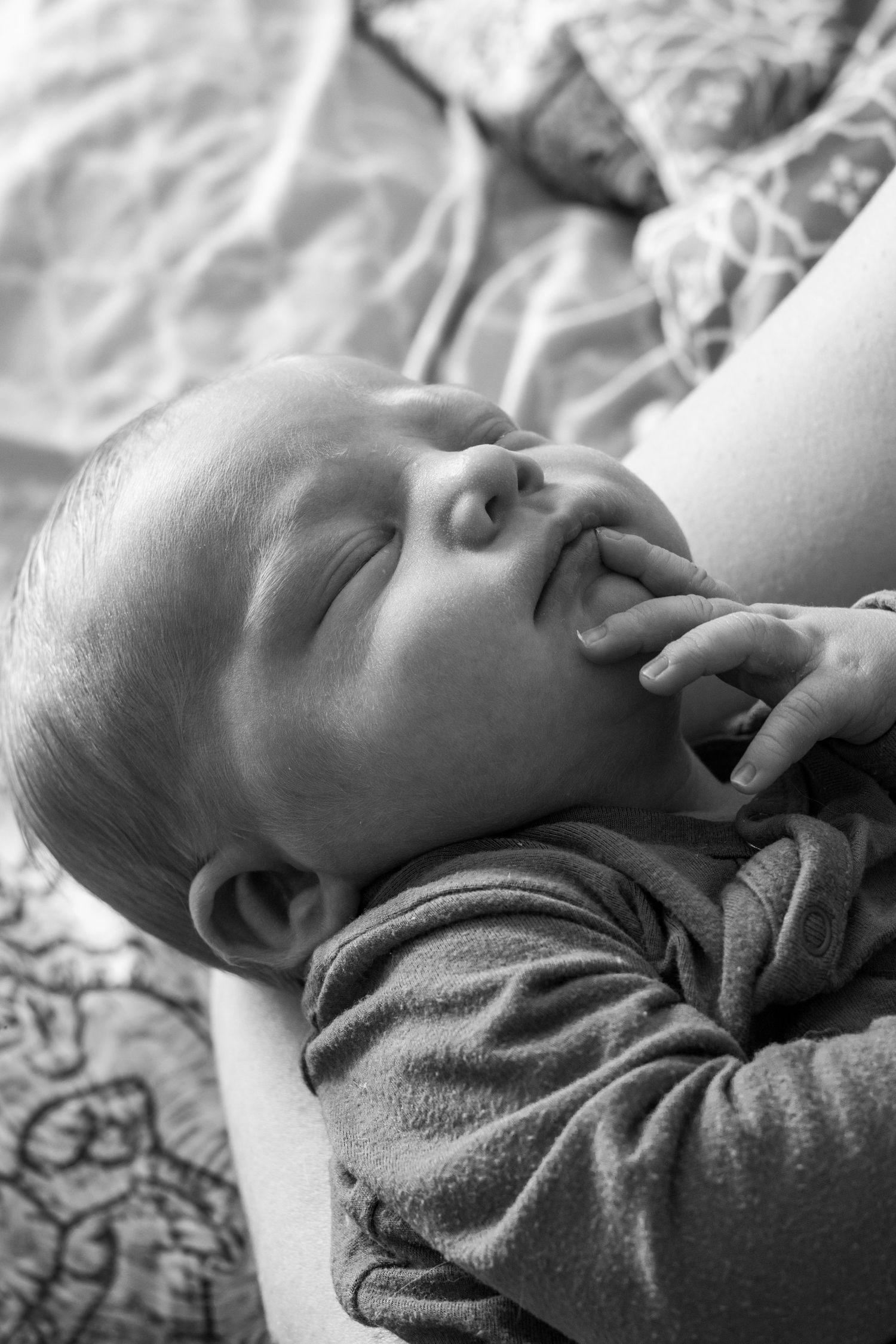 Sleeping newborn baby with hand on cheek, cradled by mother, black and white photo.