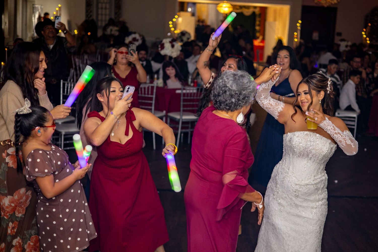 Bride and guests dance joyfully with colorful glow sticks at a lively wedding reception.