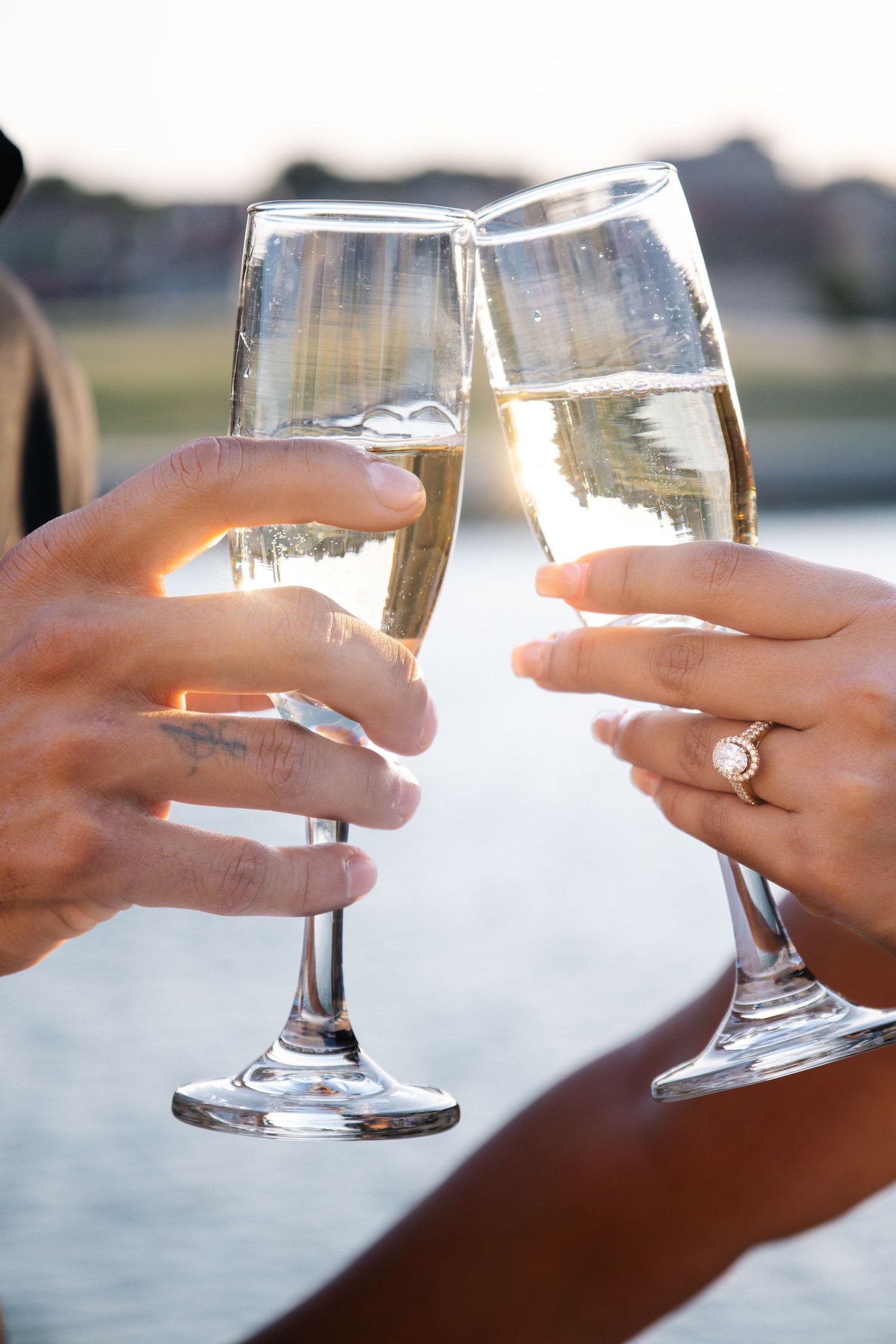 Close-up of couple toasting with champagne flutes, engagement ring visible on womans hand.