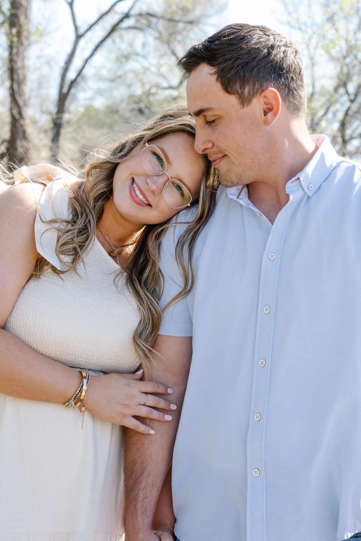 Smiling couple embracing outdoors with trees in background during engagement session.