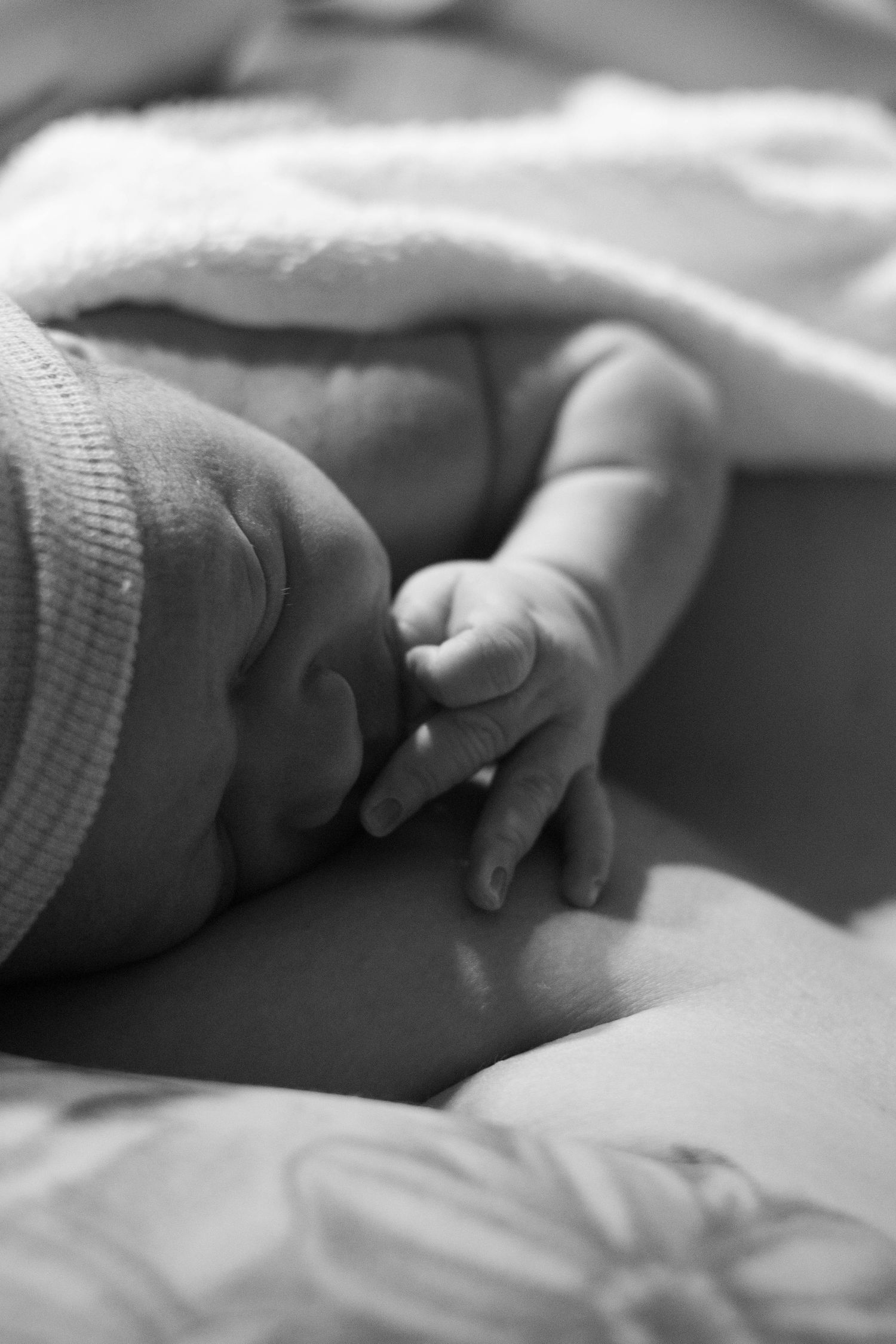 Close-up black and white photo of a sleeping newborn baby's tiny hand resting gently.
