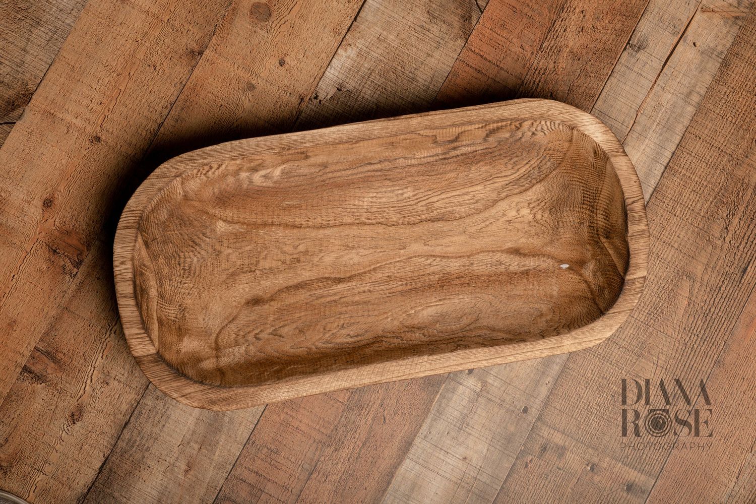 Rustic oval wooden dough bowl with natural wood grain texture, displayed on a reclaimed wood surface.