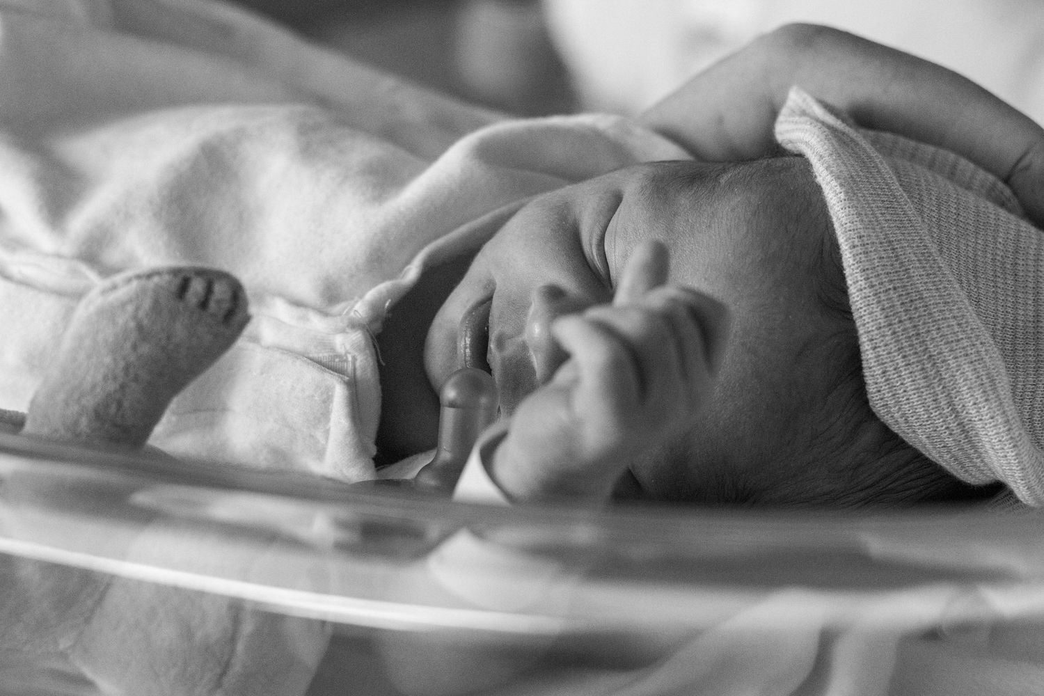 Black and white photo of a peaceful newborn baby resting in a hospital bassinet.