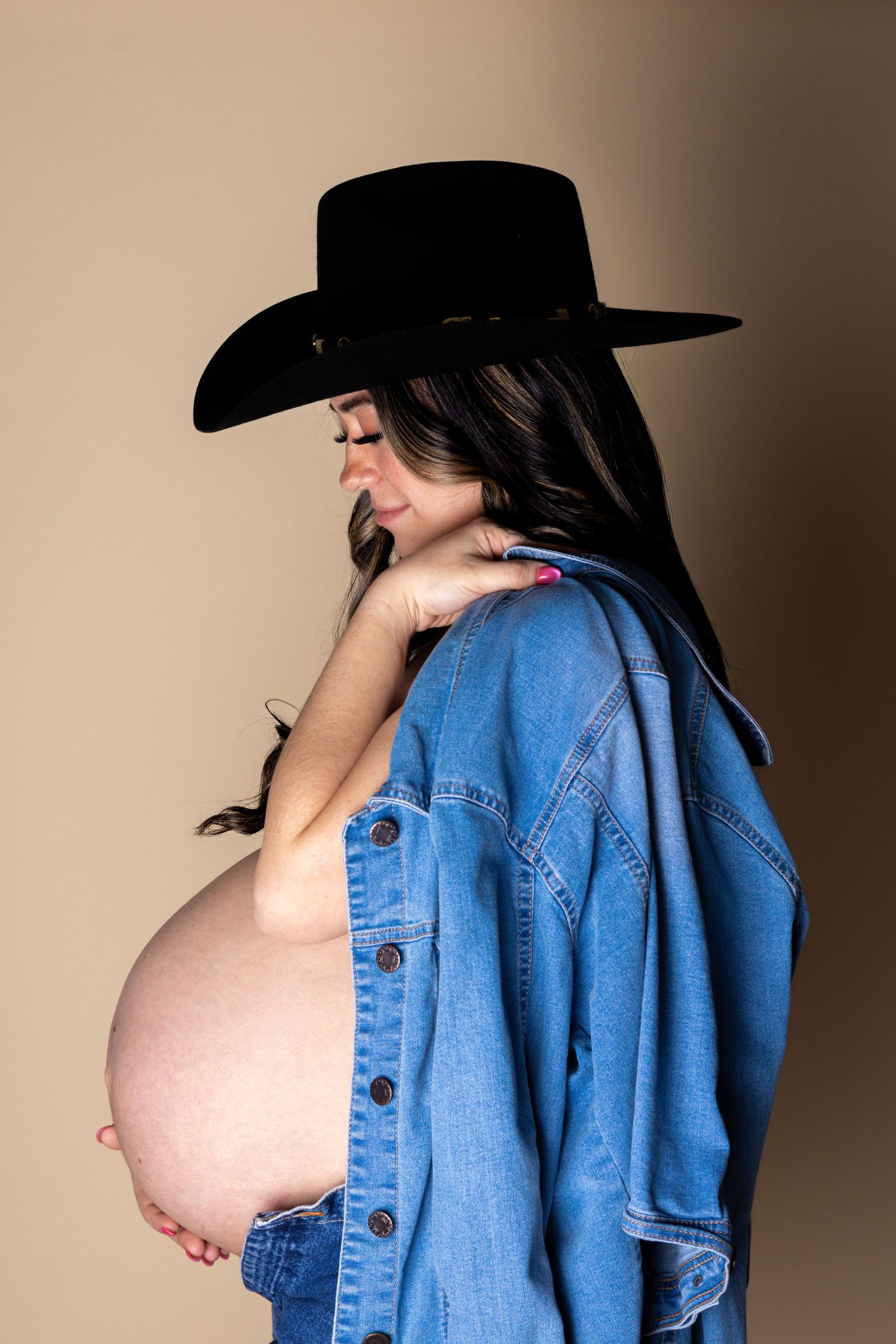Side view of pregnant woman in black cowboy hat and denim jacket, showcasing baby bump.