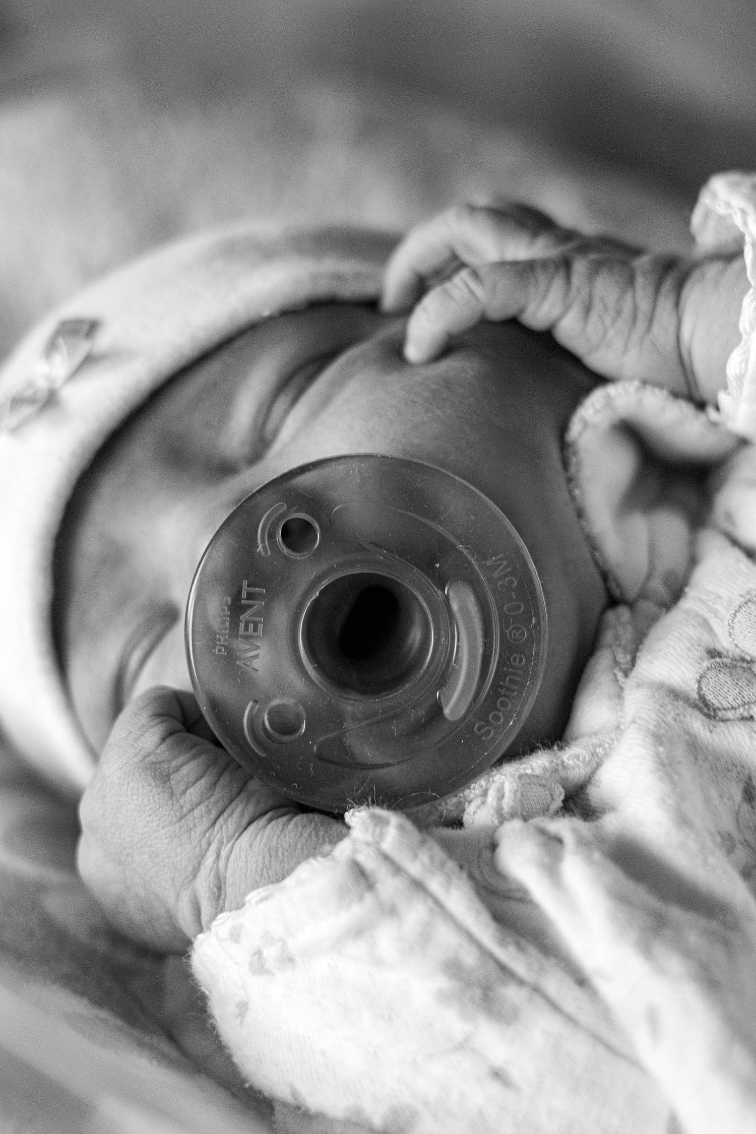 Close-up black and white photo of a sleeping newborn with a pacifier and tiny fingers visible.
