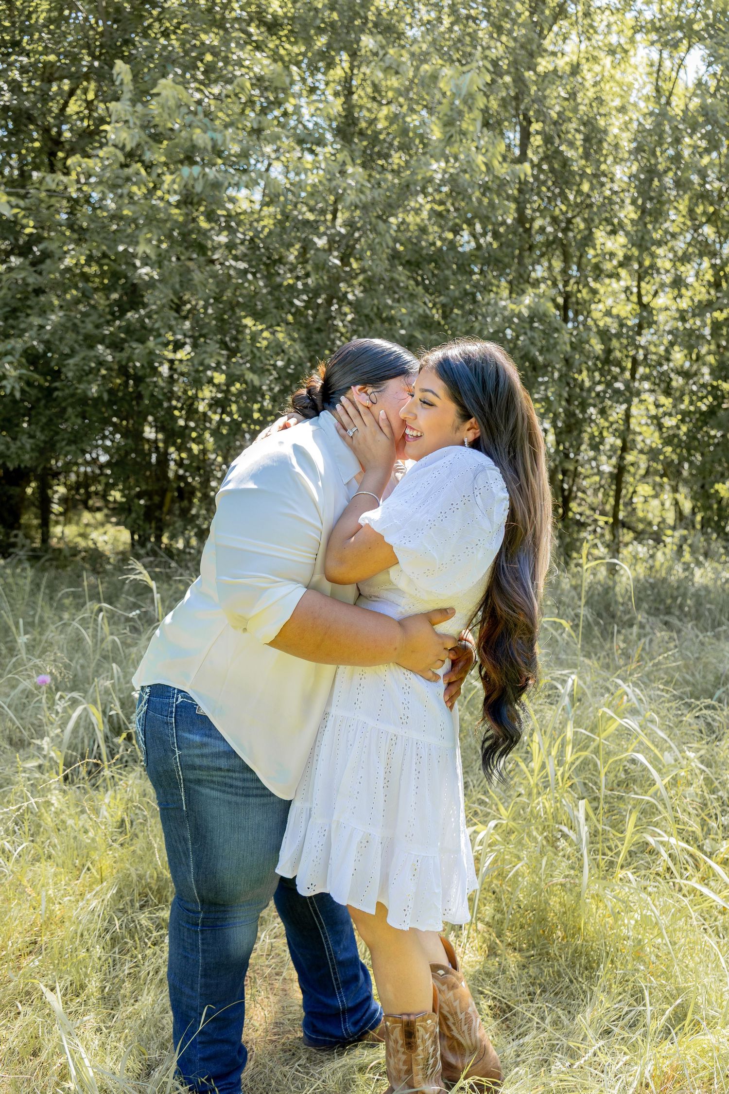 Couple hugging and laughing together in a golden sunlit grassy field.