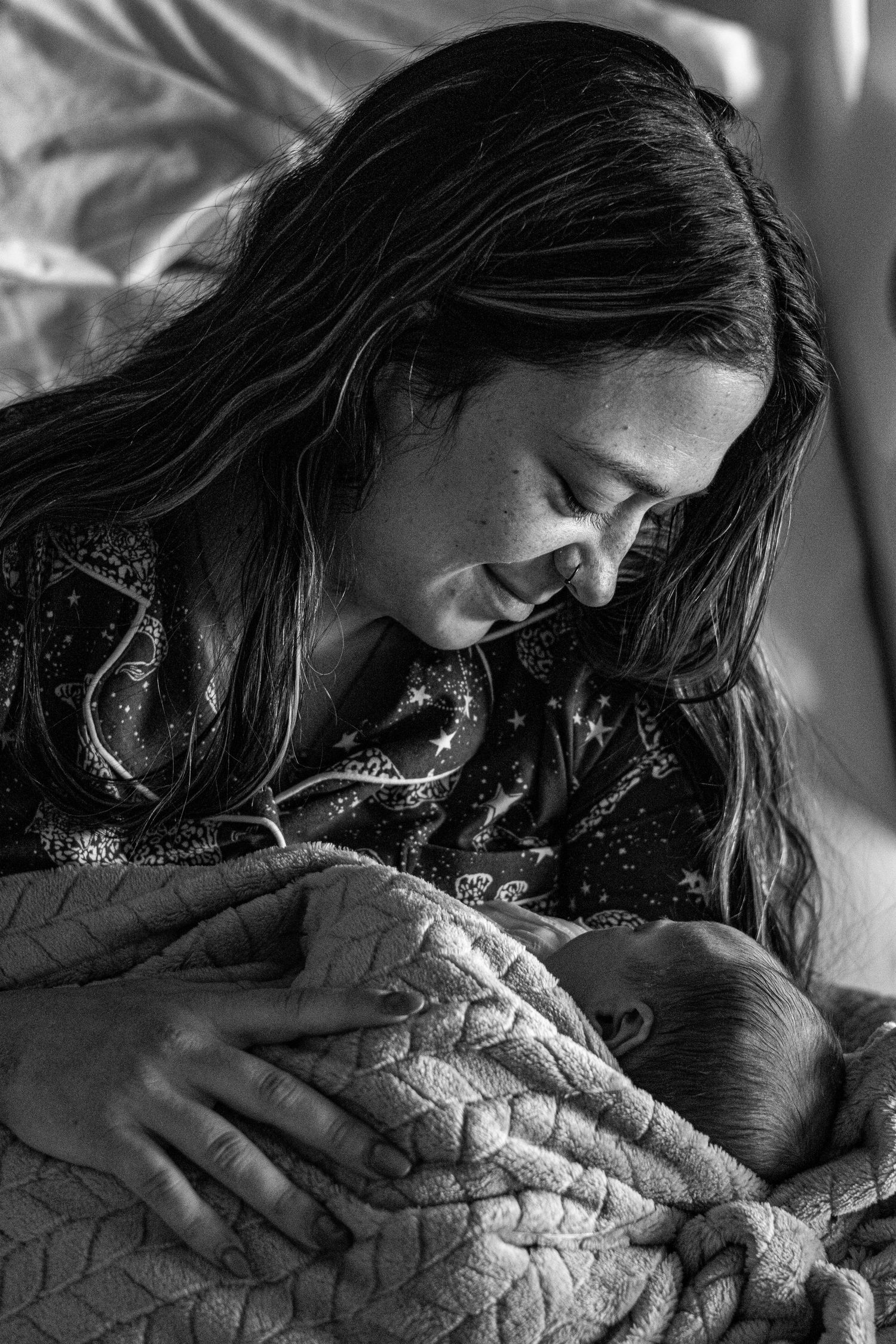 New mother with long hair smiling while holding swaddled newborn, black and white.
