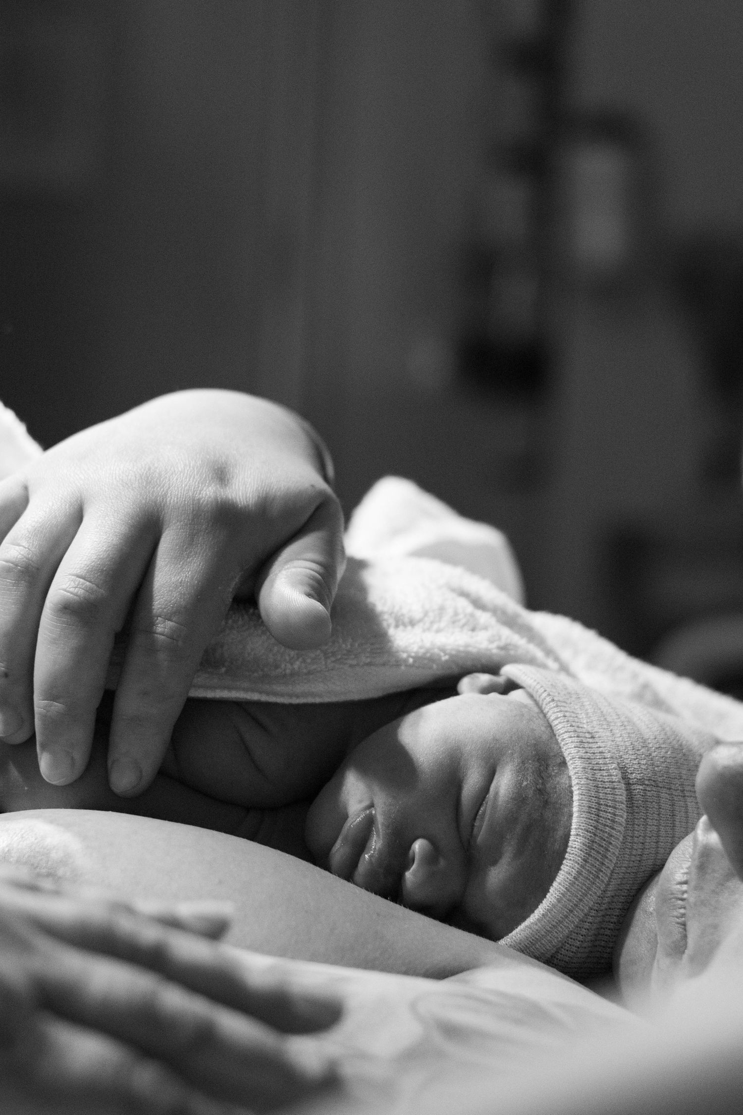 A parent gently cradles a sleeping newborn baby wearing a striped hat in black and white.