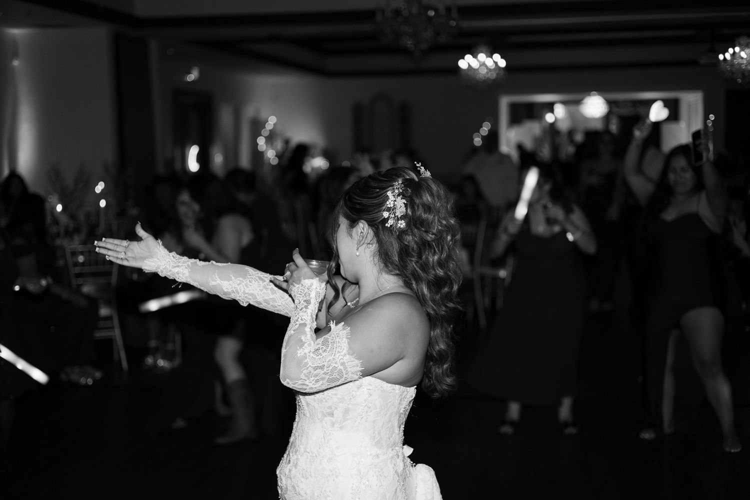 Bride in white lace gown and gloves tossing bouquet at elegant wedding reception in black and white photo.