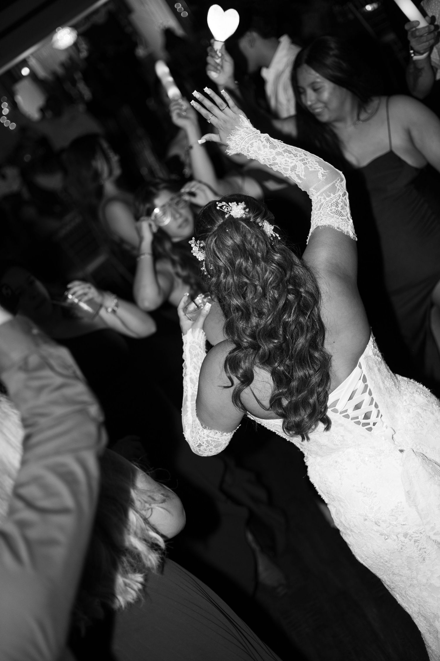 Bride dances with guests holding heart-shaped glow sticks at lively wedding reception celebration.