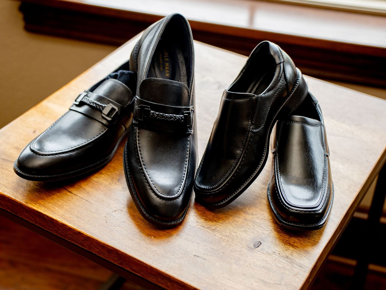 Two pairs of black leather dress loafers displayed on a wooden table, showcasing classic men's formal footwear.