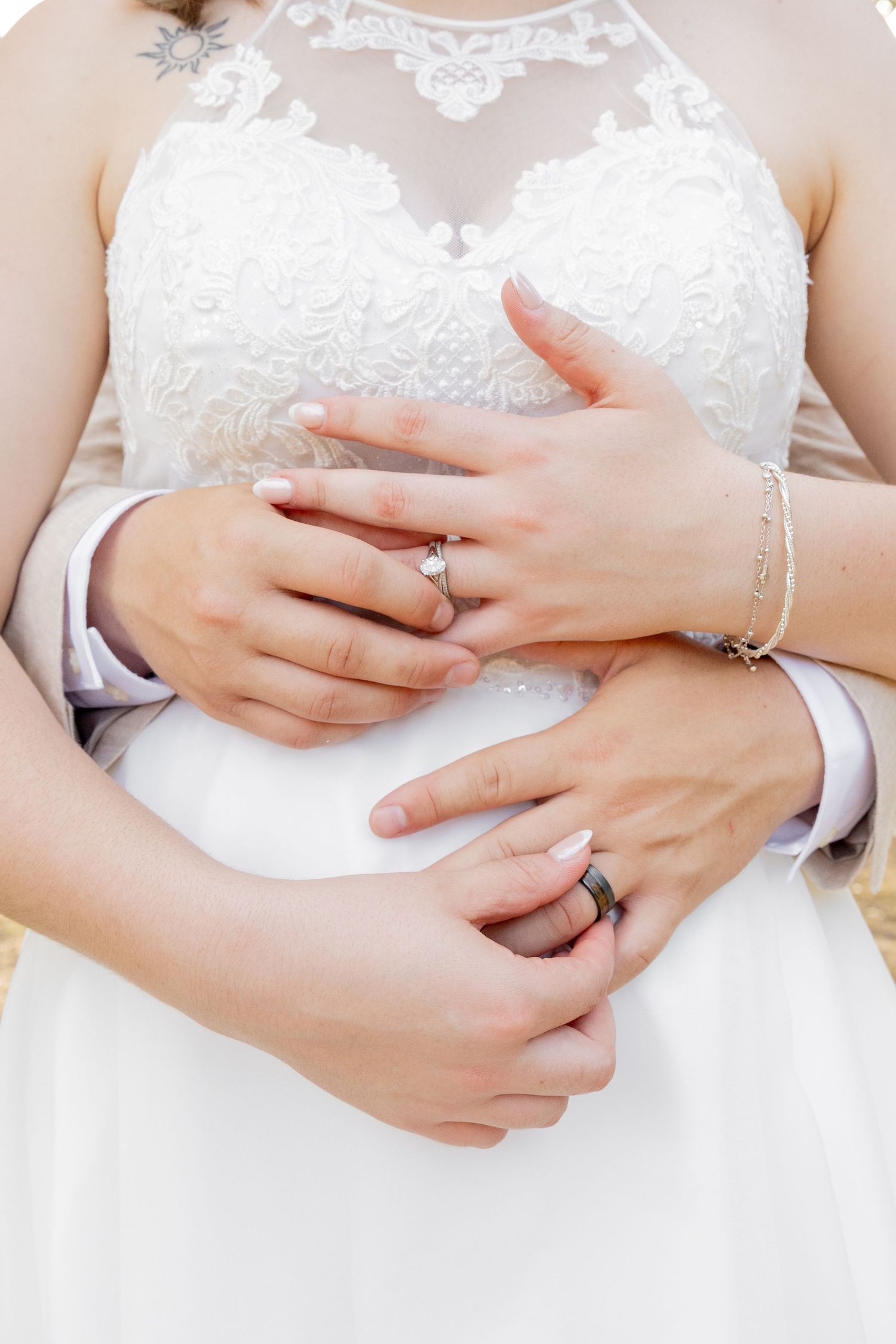 Bride and groom holding hands showing wedding rings, bride in white lace dress with bracelet on wrist.