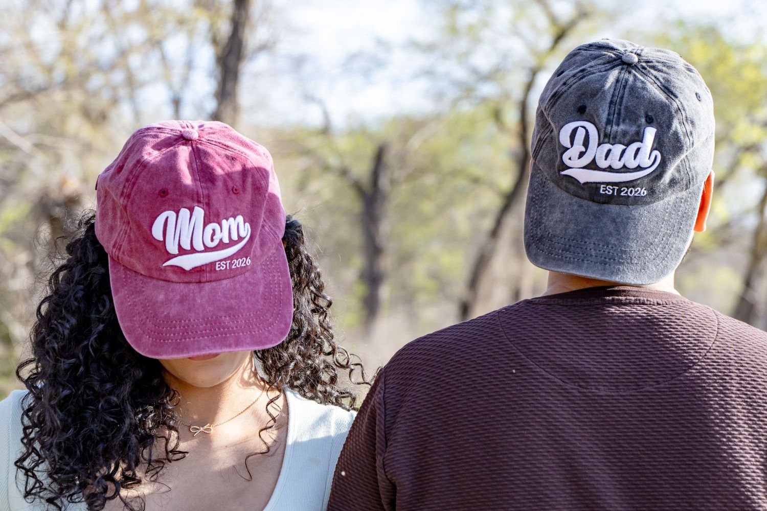 Rear view of expecting couple wearing coordinating Mom and Dad caps while standing outdoors in nature.