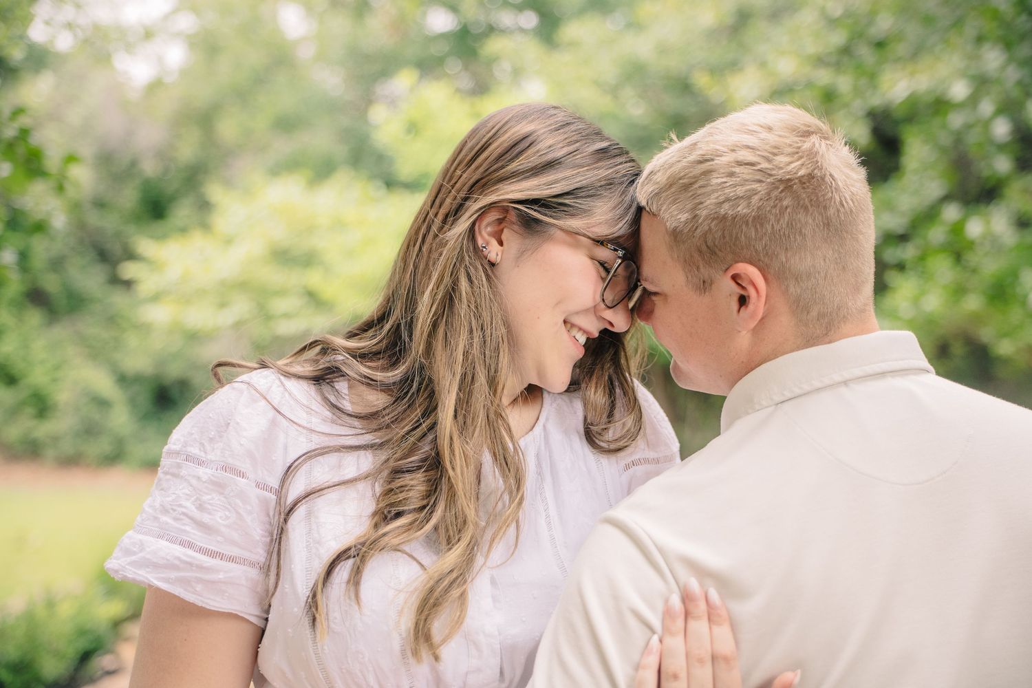 Couple sharing a romantic forehead touch outdoors, smiling woman with glasses and long hair embracing her partner.