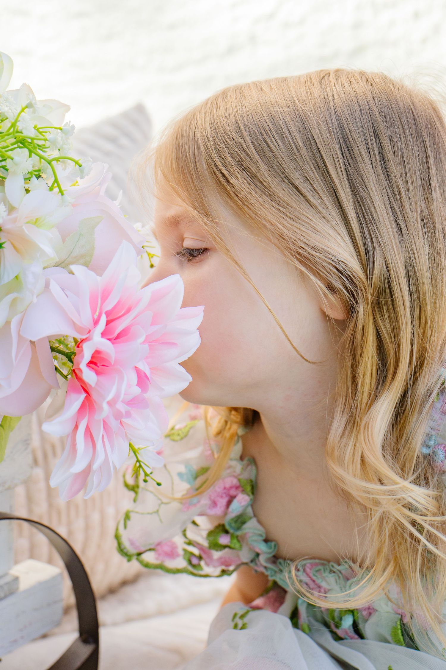 Young blonde girl smelling a large pink dahlia flower from a floral arrangement outdoors.