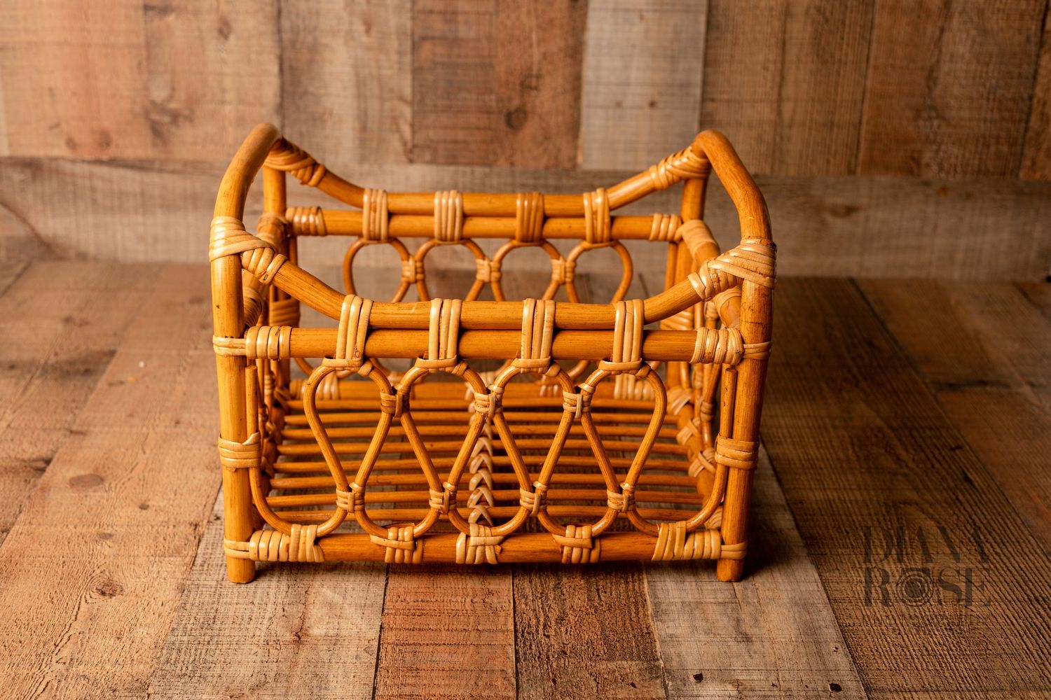 Vintage wicker rattan magazine rack basket with decorative woven pattern, natural orange-brown color, rustic wooden background.