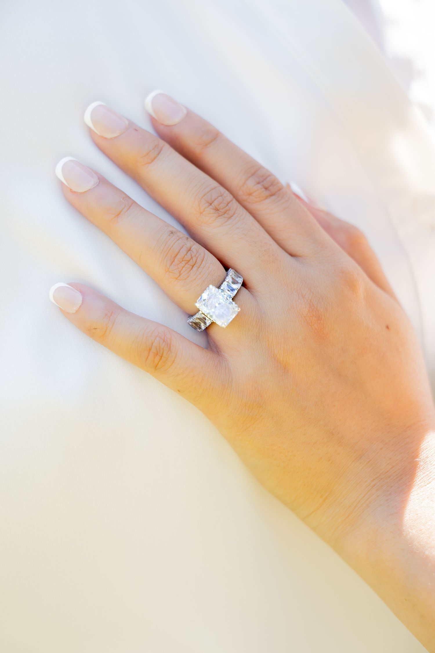 Close-up of a hand wearing a stunning emerald-cut diamond engagement ring with French manicure.