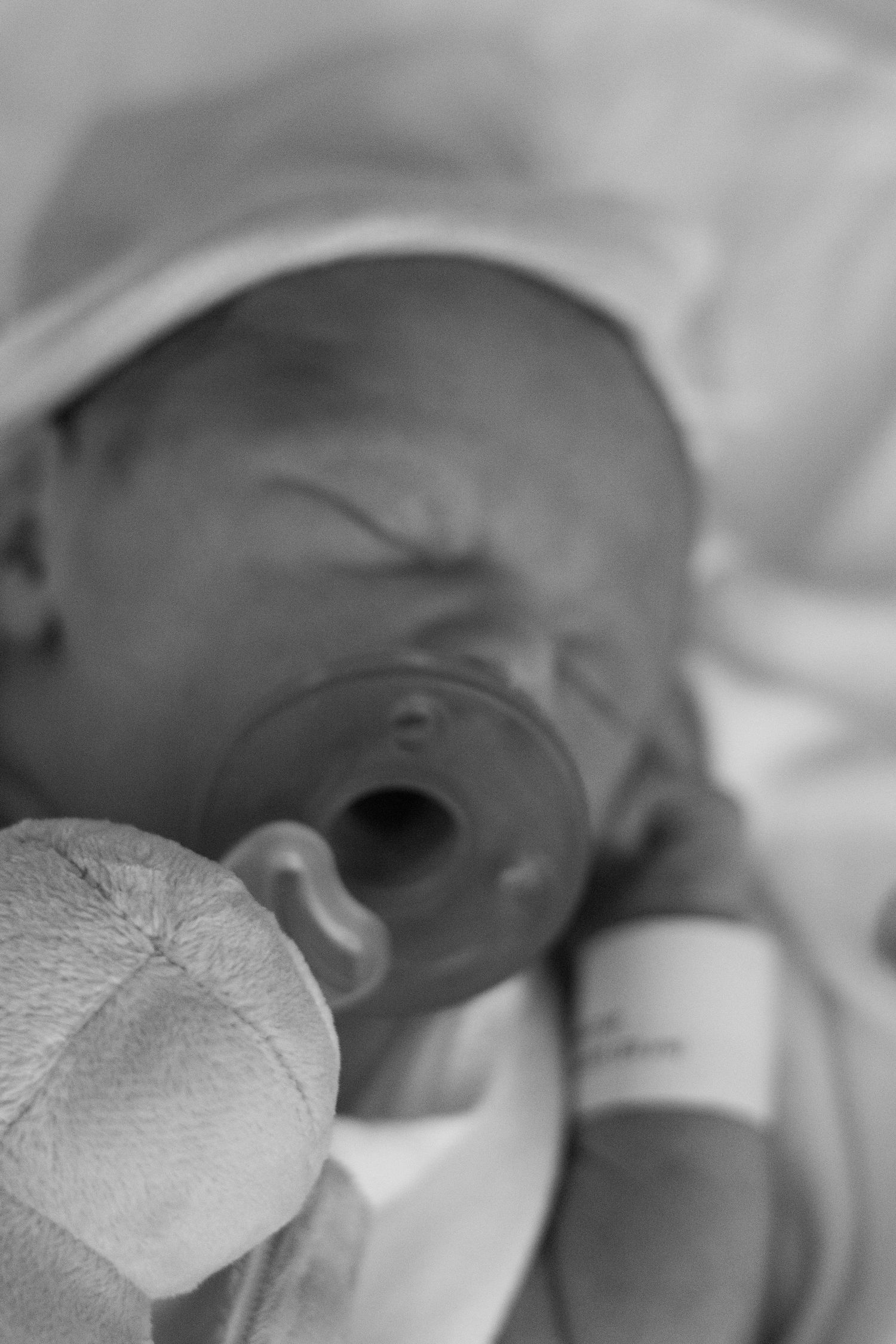 Black and white photo of a newborn baby with a pacifier wearing a hospital hat.