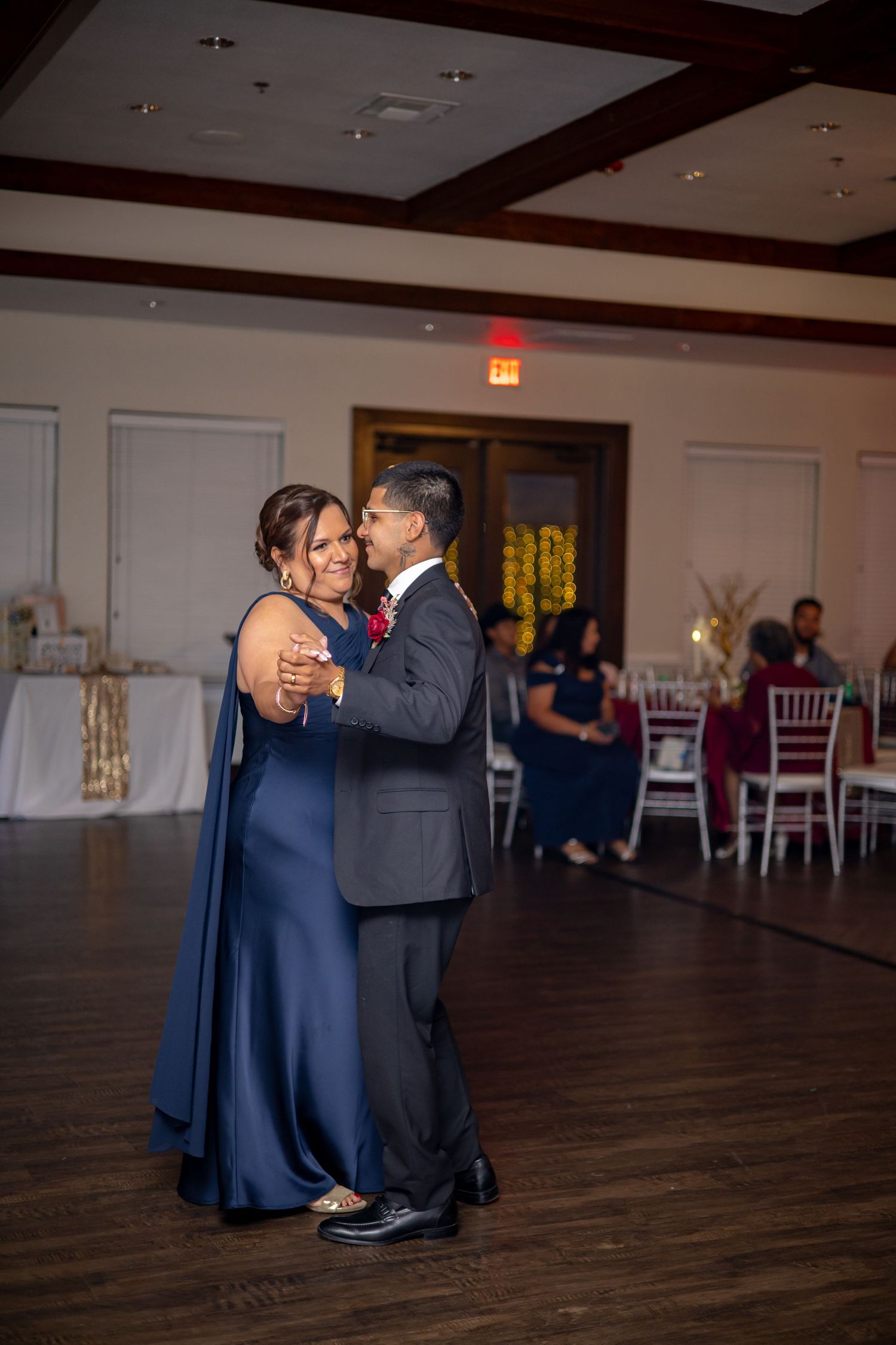 Groom dances with mother in navy gown during heartfelt mother-son dance at wedding reception.
