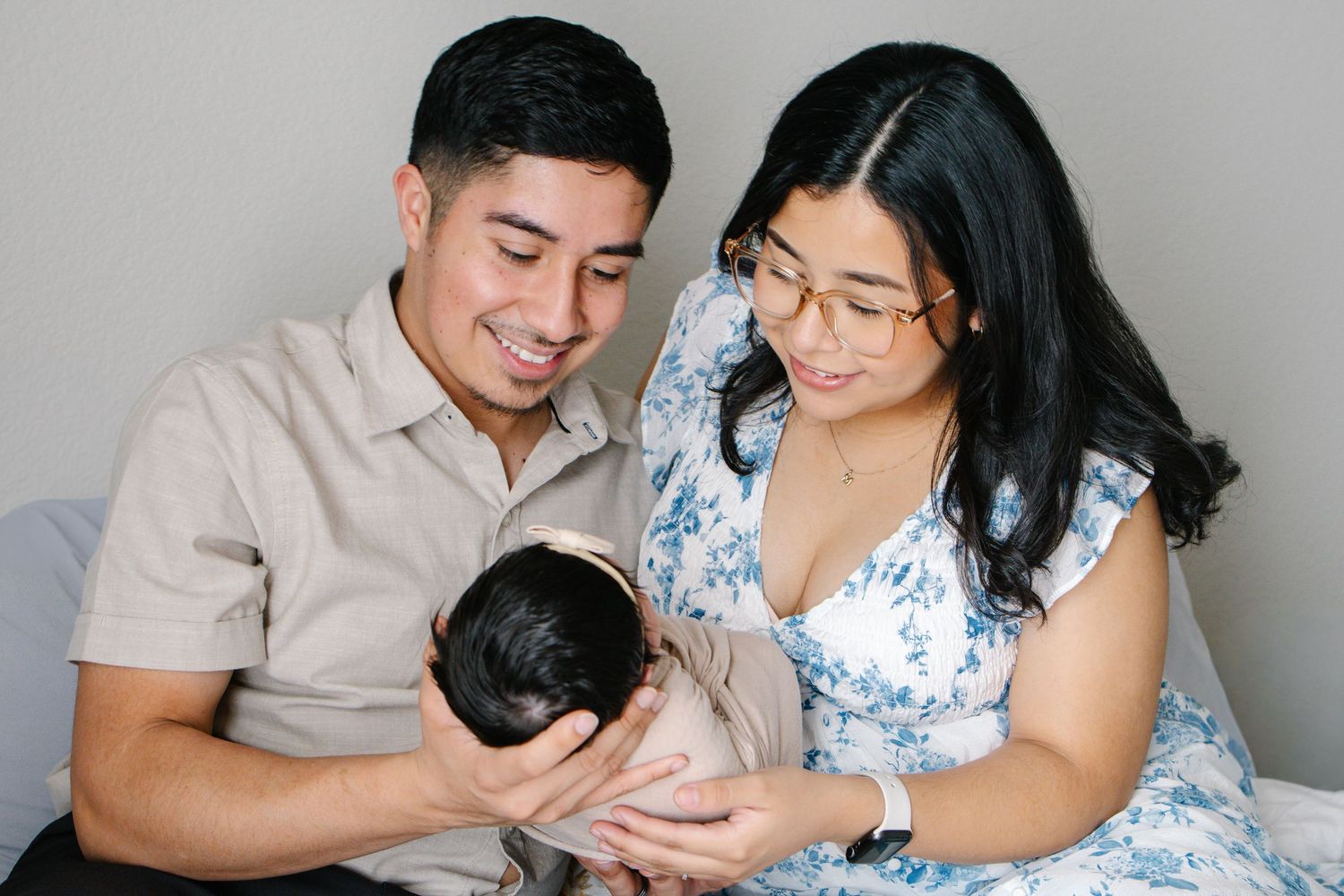 Smiling couple admiring their sleeping newborn baby during a studio portrait session.