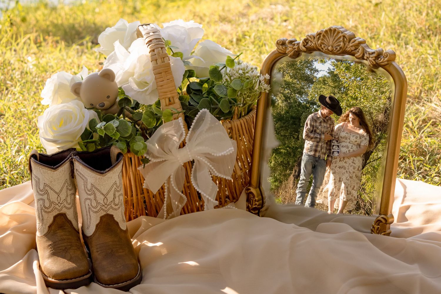 Rustic pregnancy announcement with cowboy boots, white roses in a basket, and couple reflected in a vintage mirror outdoors.