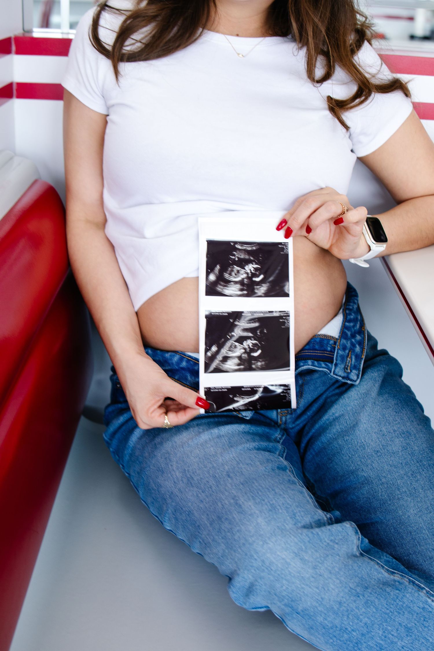 Close-up of pregnant woman's baby bump as she holds ultrasound photos while seated in an In-N-Out Burger booth.