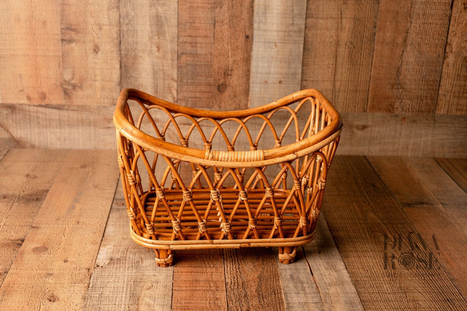 Vintage wicker rattan baby bassinet with diamond lattice design and small feet on rustic wood background.