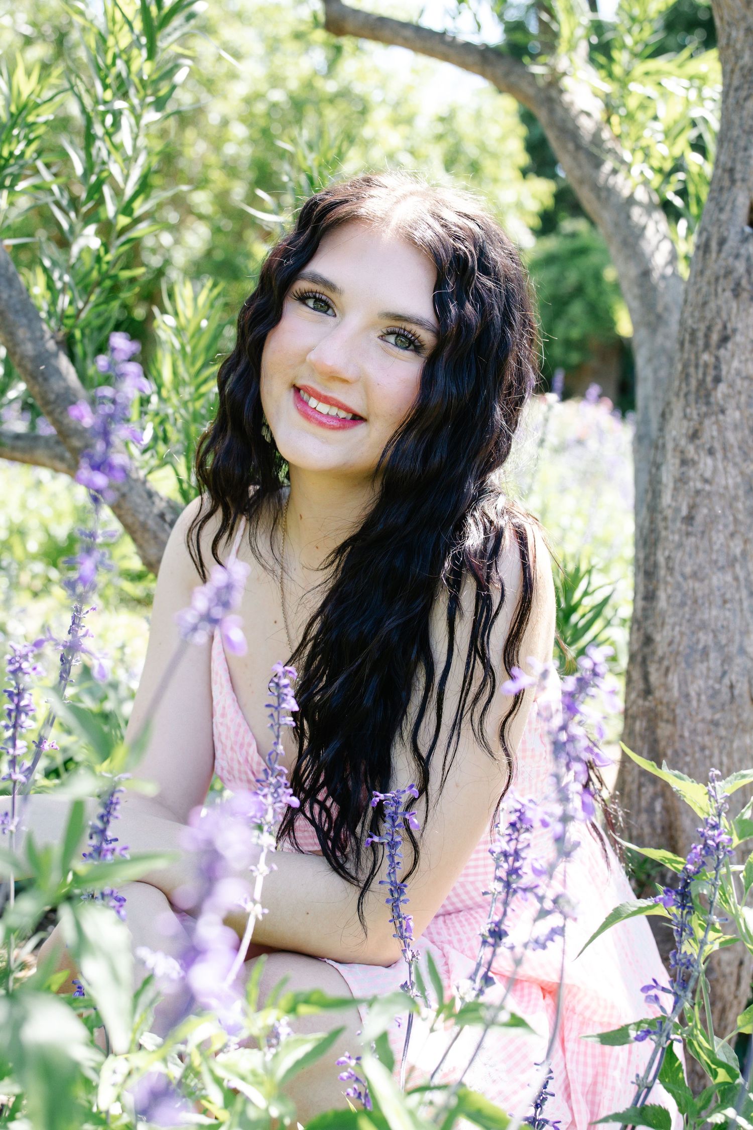 Beautiful young woman with dark hair smiling among purple lavender flowers in a sunny garden.
