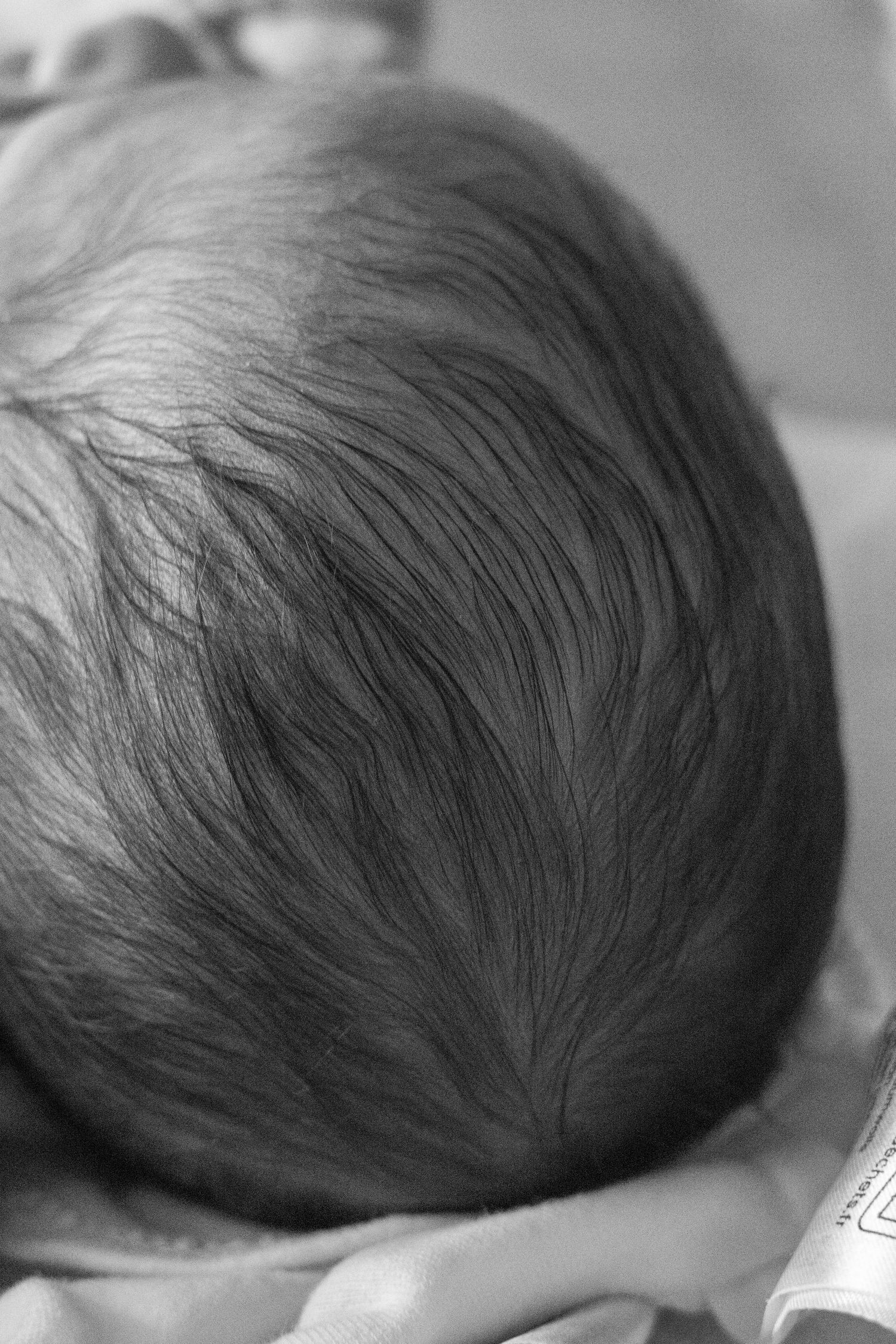 Close-up black and white photo showcasing a newborn baby's full head of dark hair.