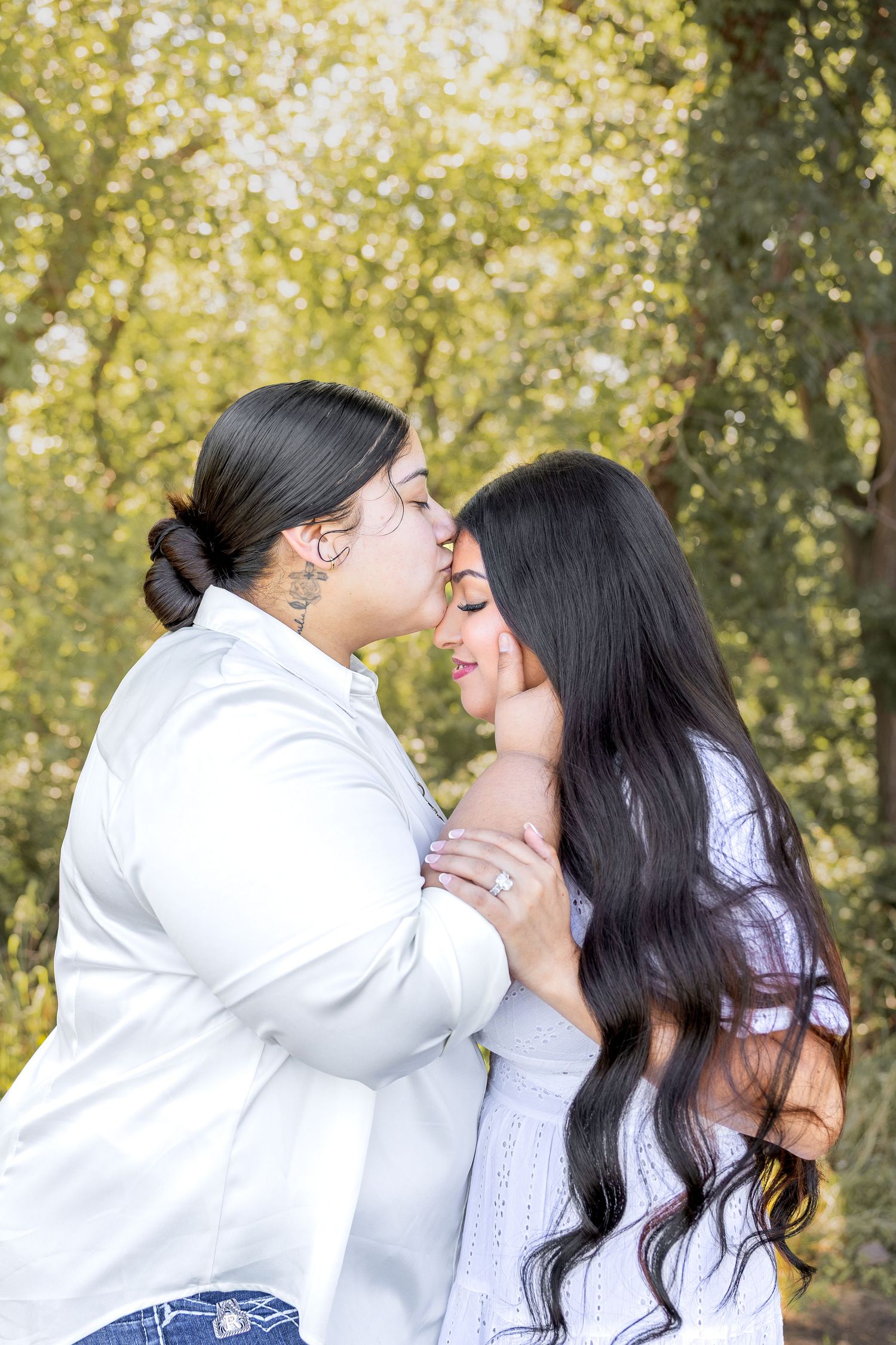 Couple embracing and sharing an intimate moment surrounded by green trees outdoors.