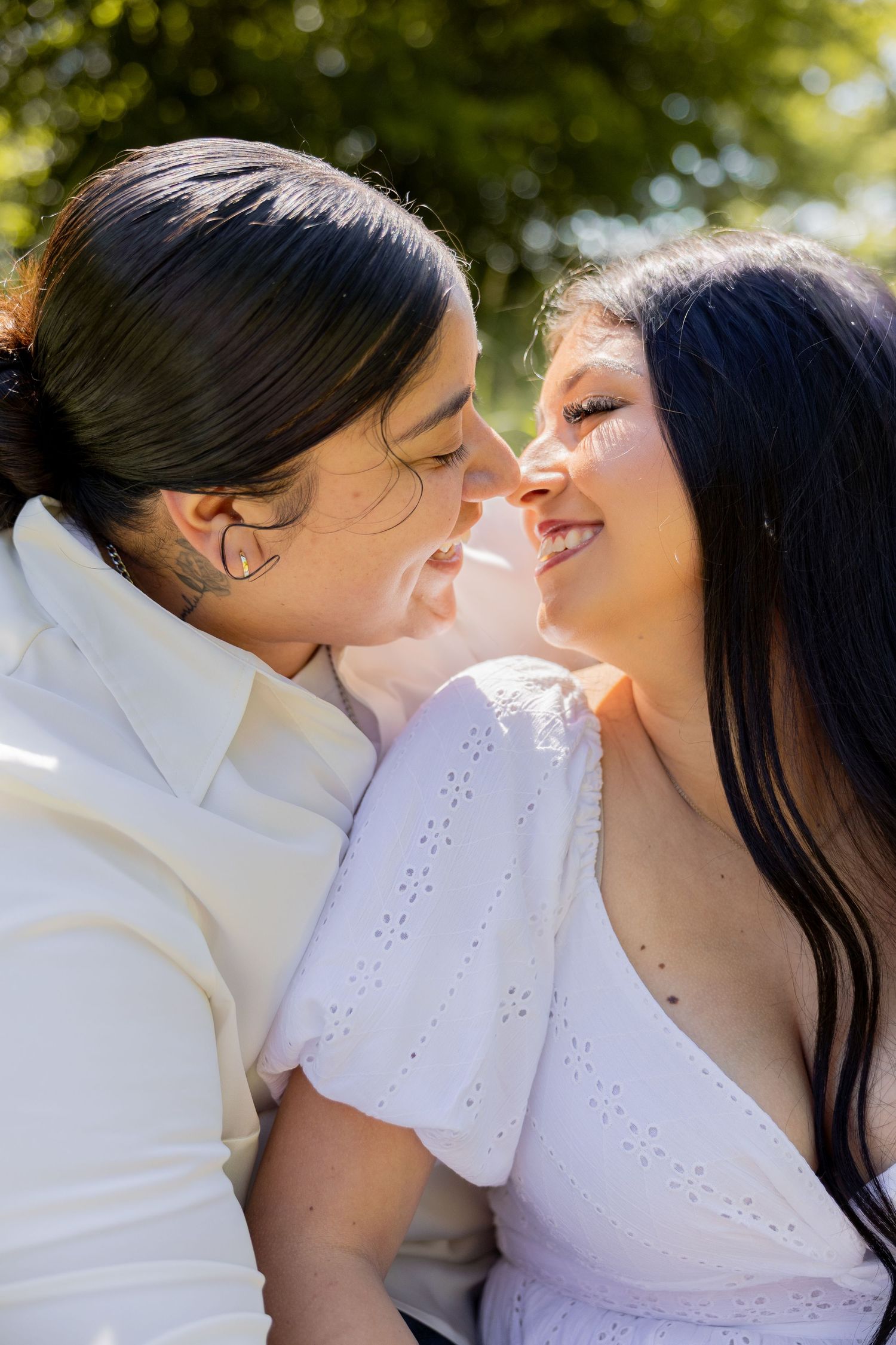 Romantic close-up of a couple leaning in for a kiss outdoors with lush green trees in the background.