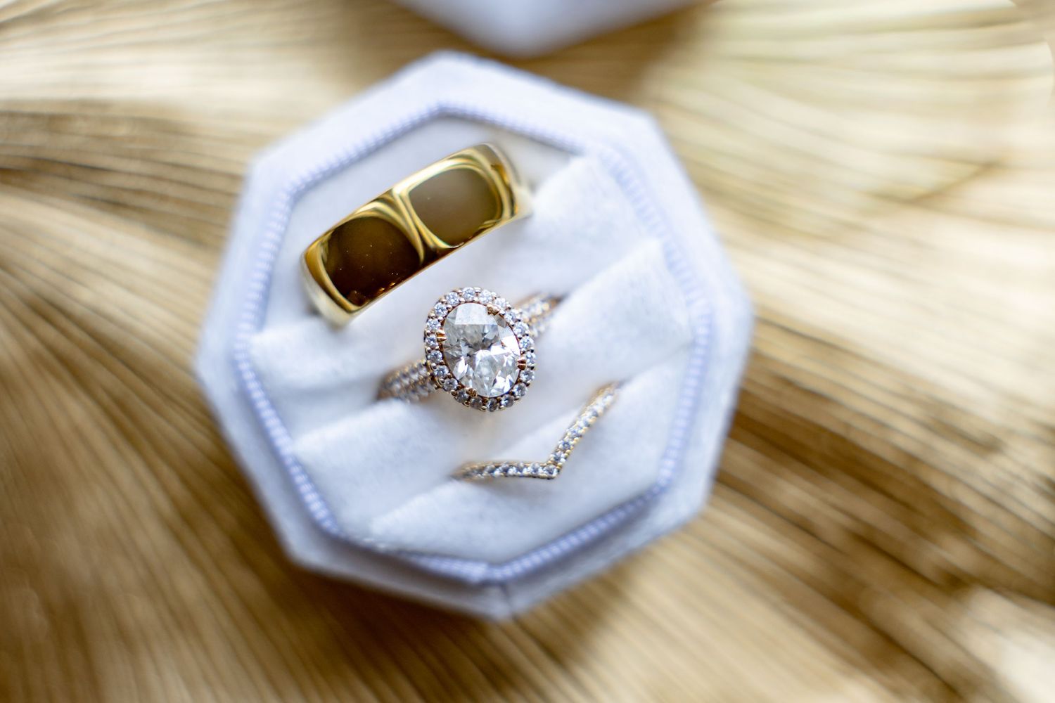 Elegant wedding ring set with oval diamond halo engagement ring and gold band displayed in a white velvet ring box.