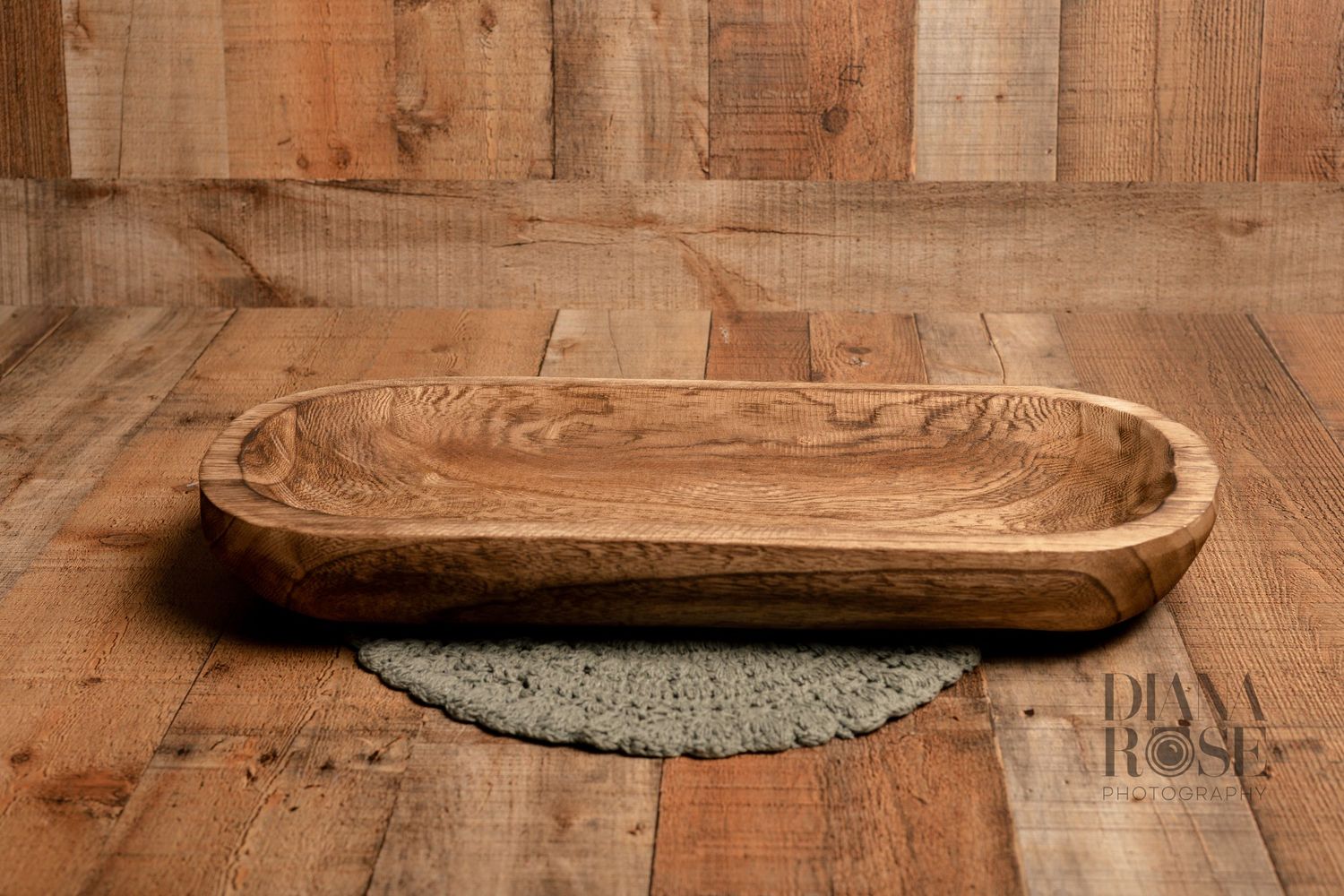 Rustic wooden oval dough bowl on a woven mat against a reclaimed wood backdrop.