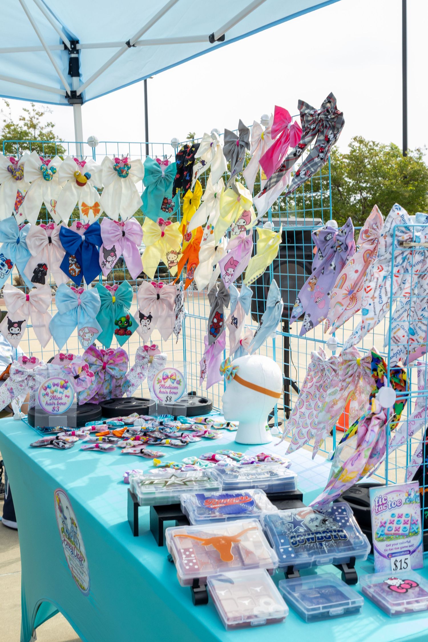 Colorful hair bows and accessories displayed on a teal table at an outdoor craft fair vendor booth.