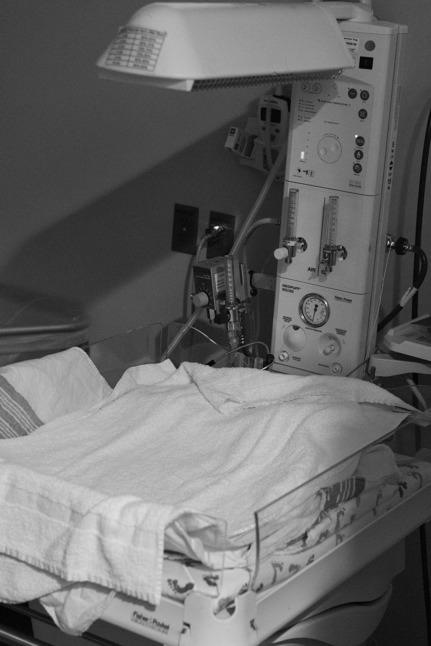 A newborn baby warmer with white blankets under a heat lamp in a hospital delivery room.