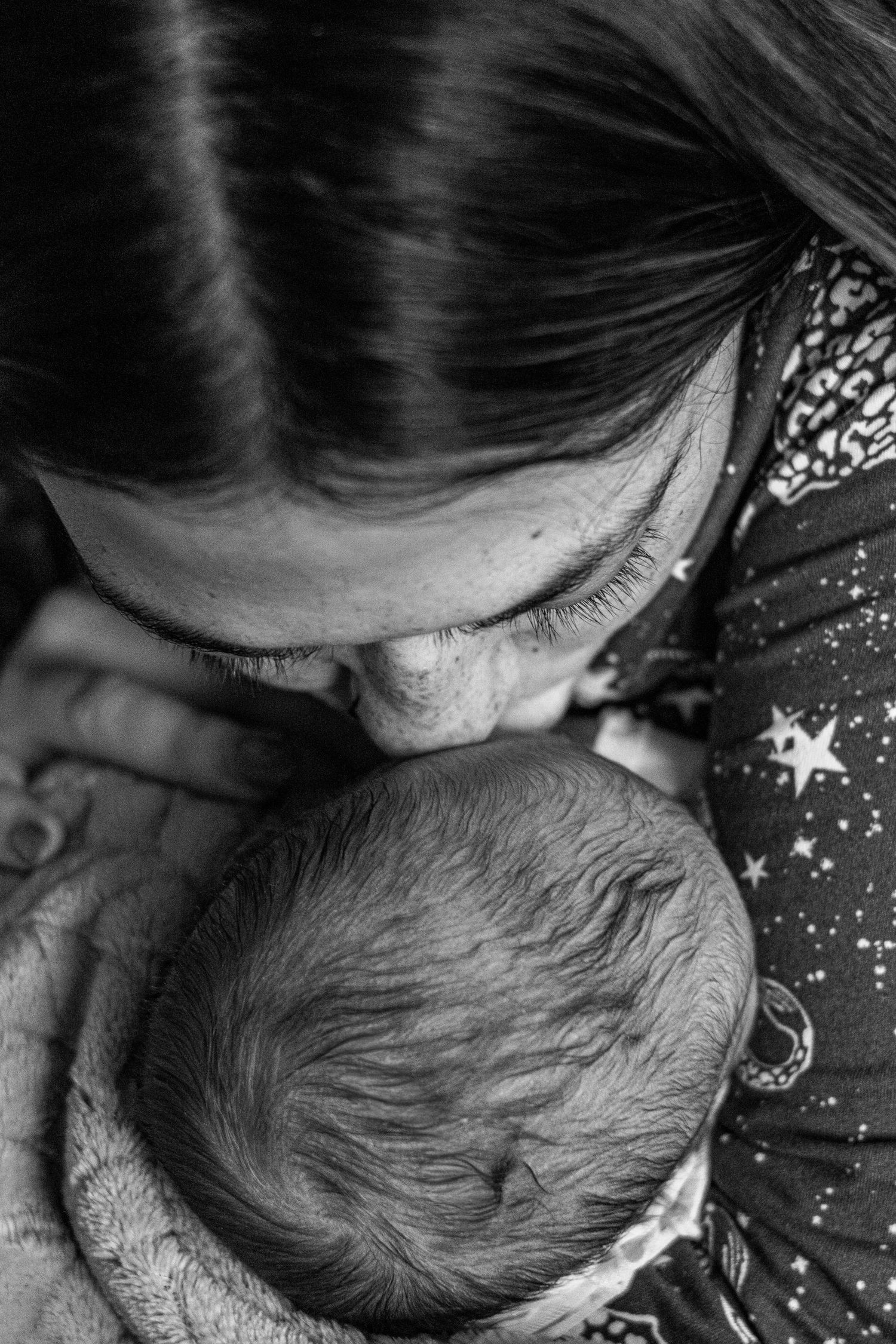 Mother tenderly kissing newborn baby\u2019s head in hospital, black and white photography.