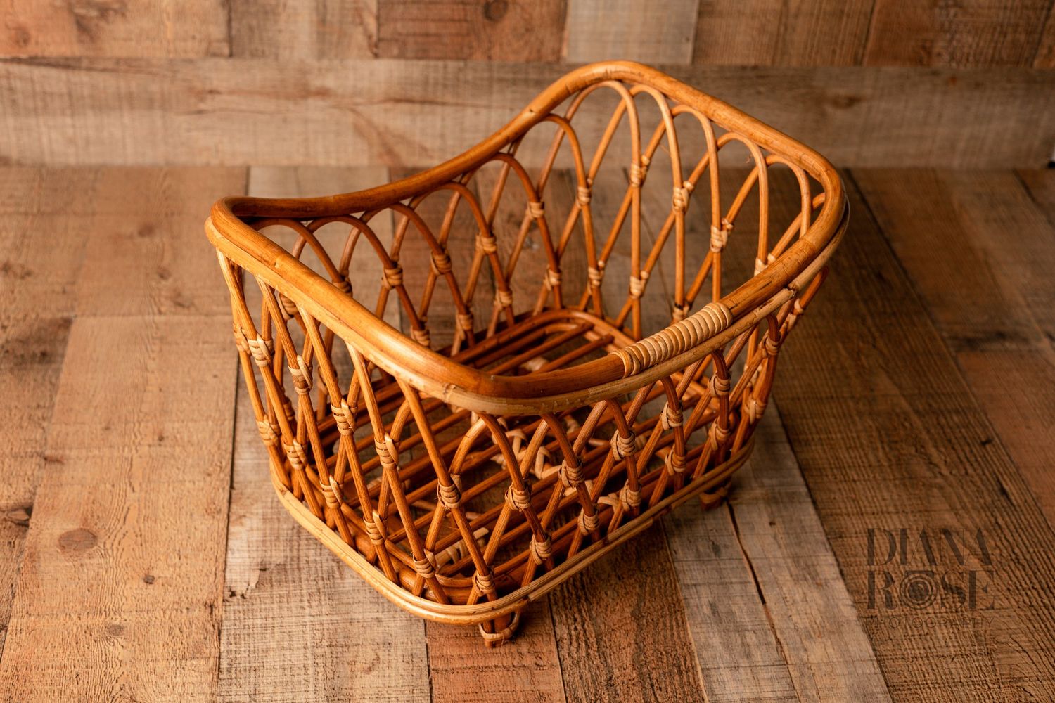 Handwoven rattan wicker basket with open lattice sides and curved handles on a rustic wood background.