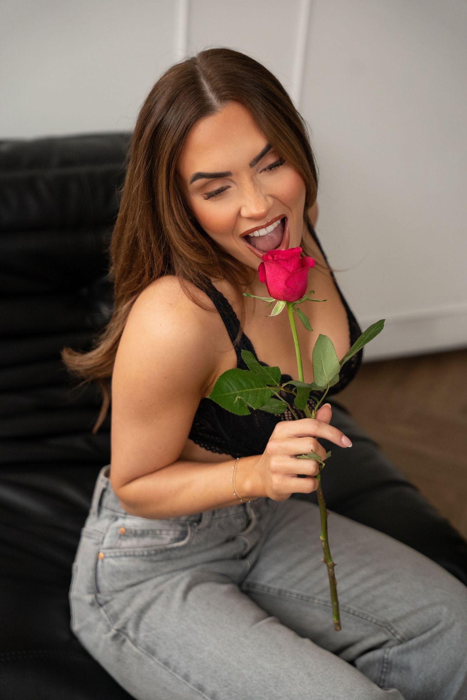 Smiling woman in black bralette and jeans holding a red rose.
