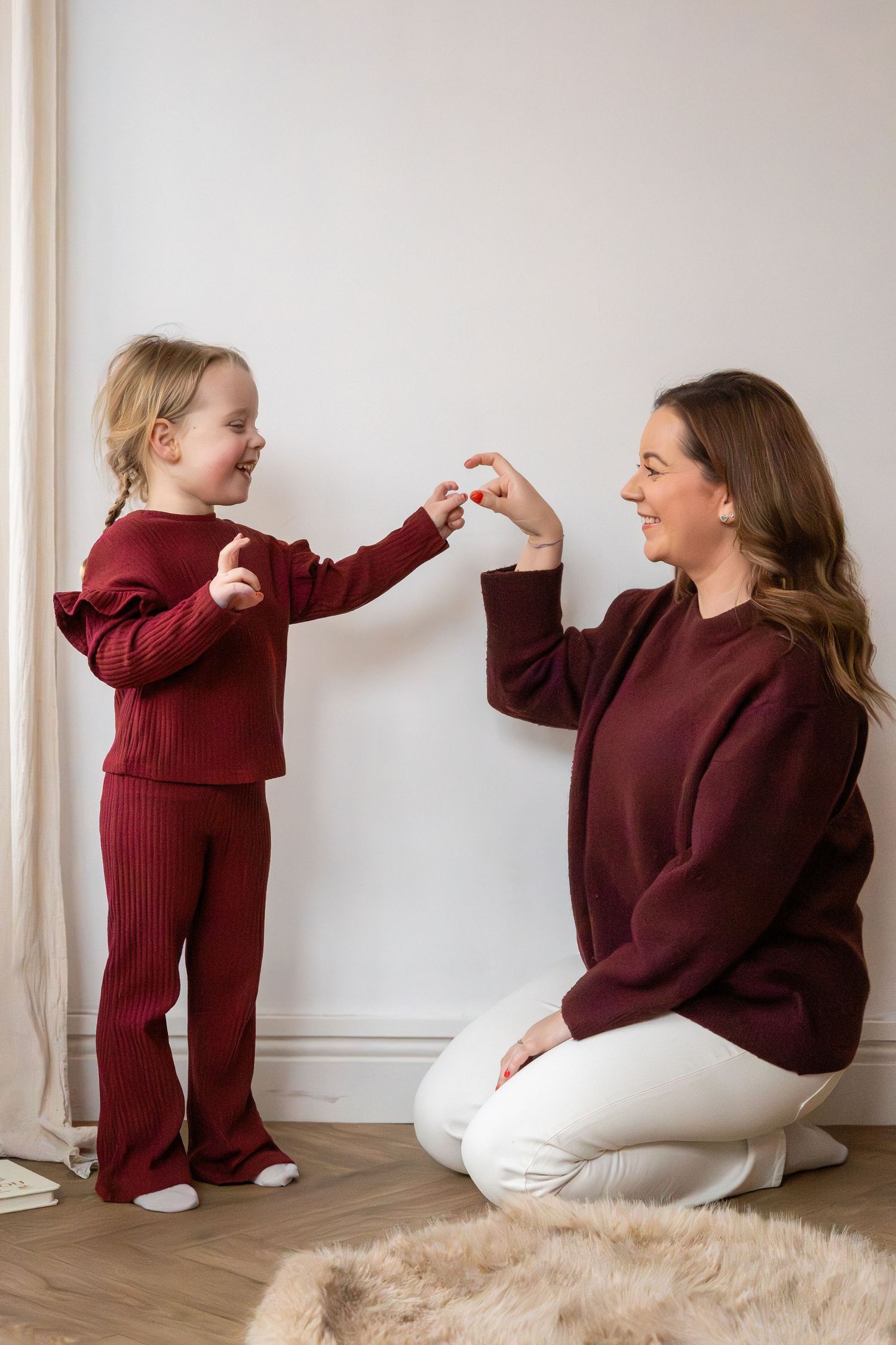 A mother and young daughter in matching burgundy outfits play together on the floor.