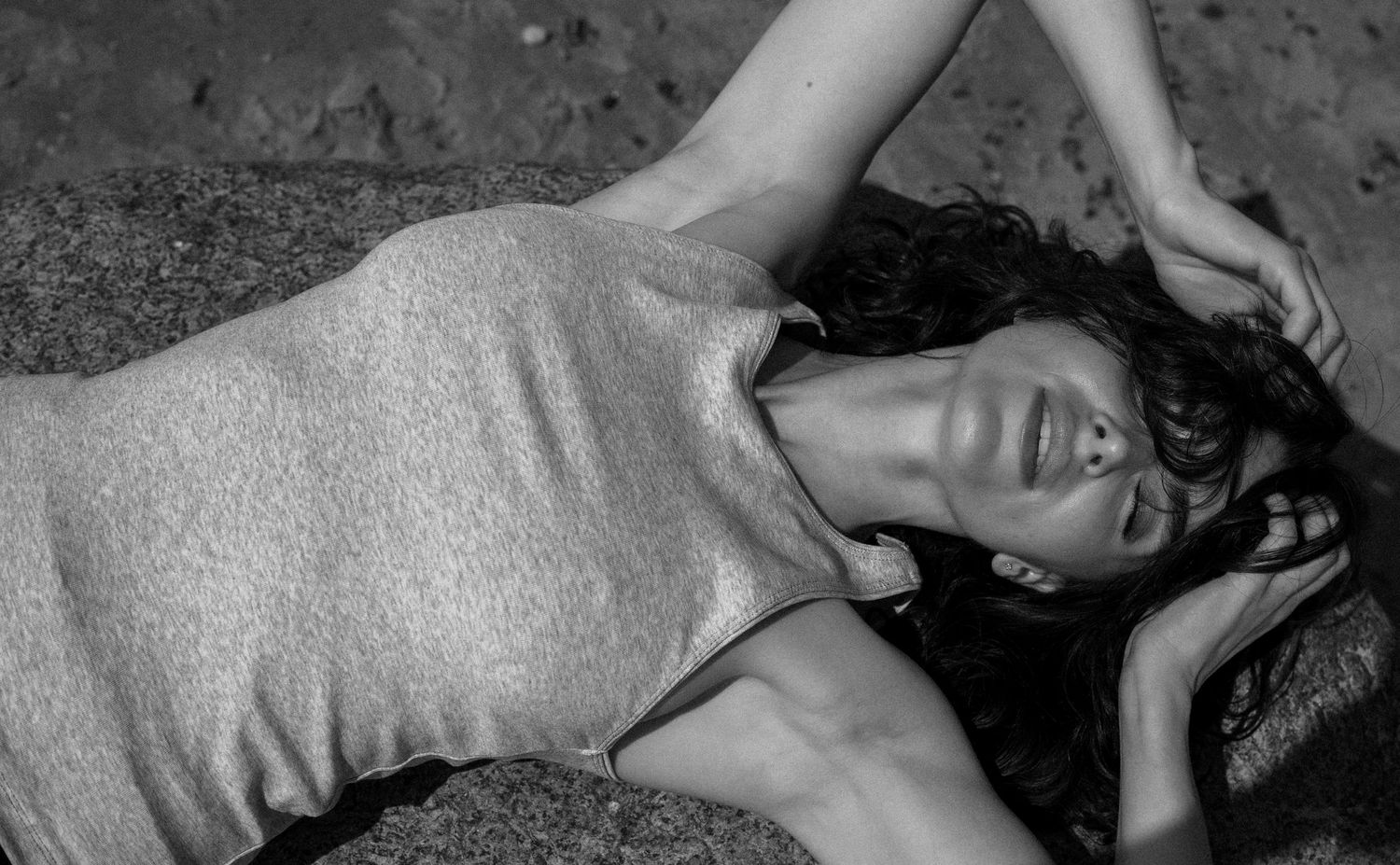 Black and white photo of woman lying on ground in sleeveless dress with hand in hair.